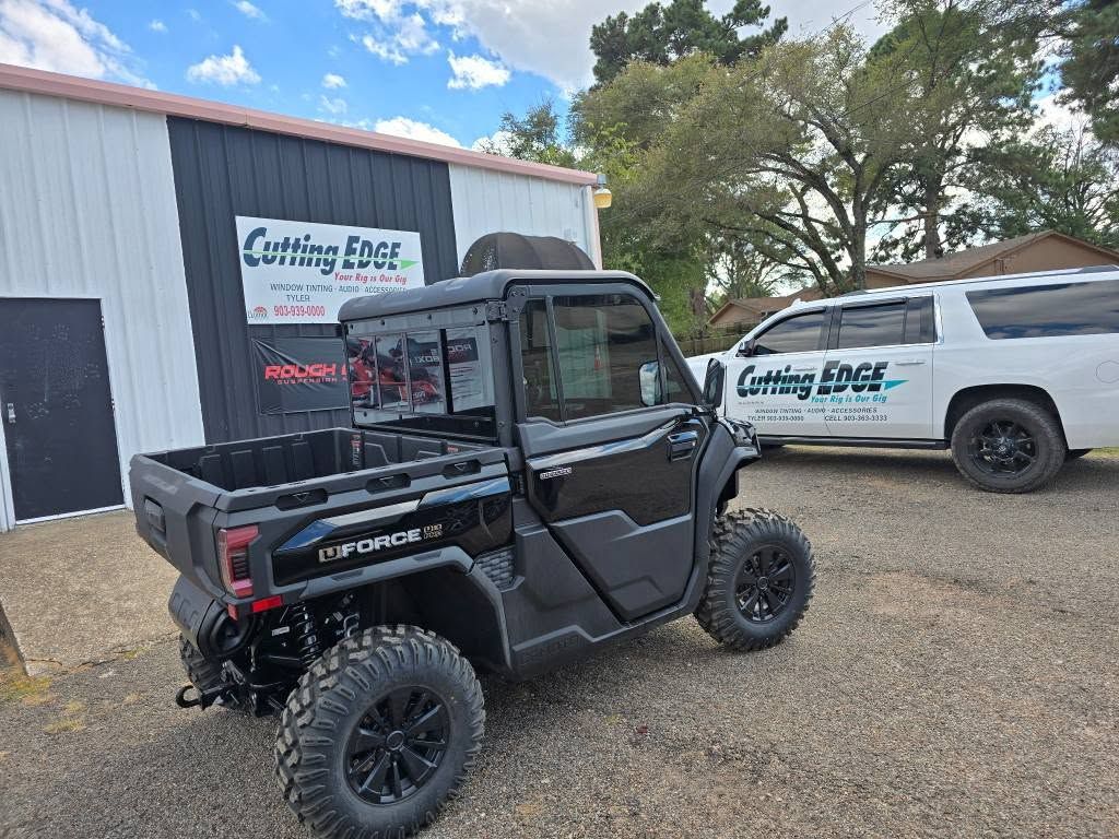 Black utility side-by-side parked outside a shop with a white service truck in the background