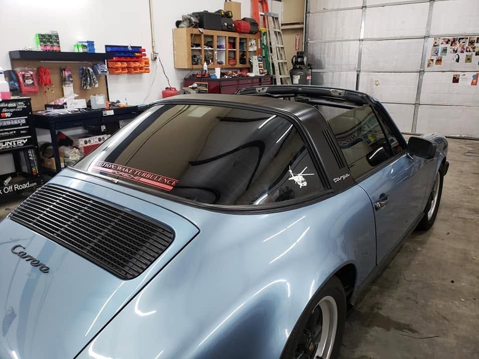 Light blue Porsche coupe in a garage, seen from the rear side with black tinted windows and spoiler.