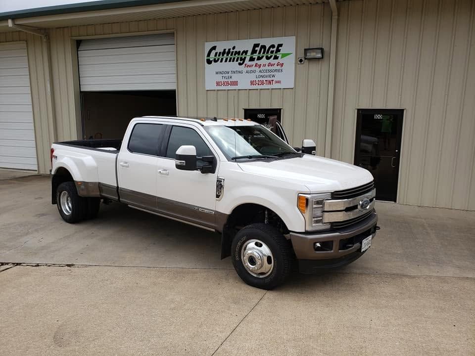 White heavy-duty pickup truck parked outside a custom truck shop with a beige metal building behind it