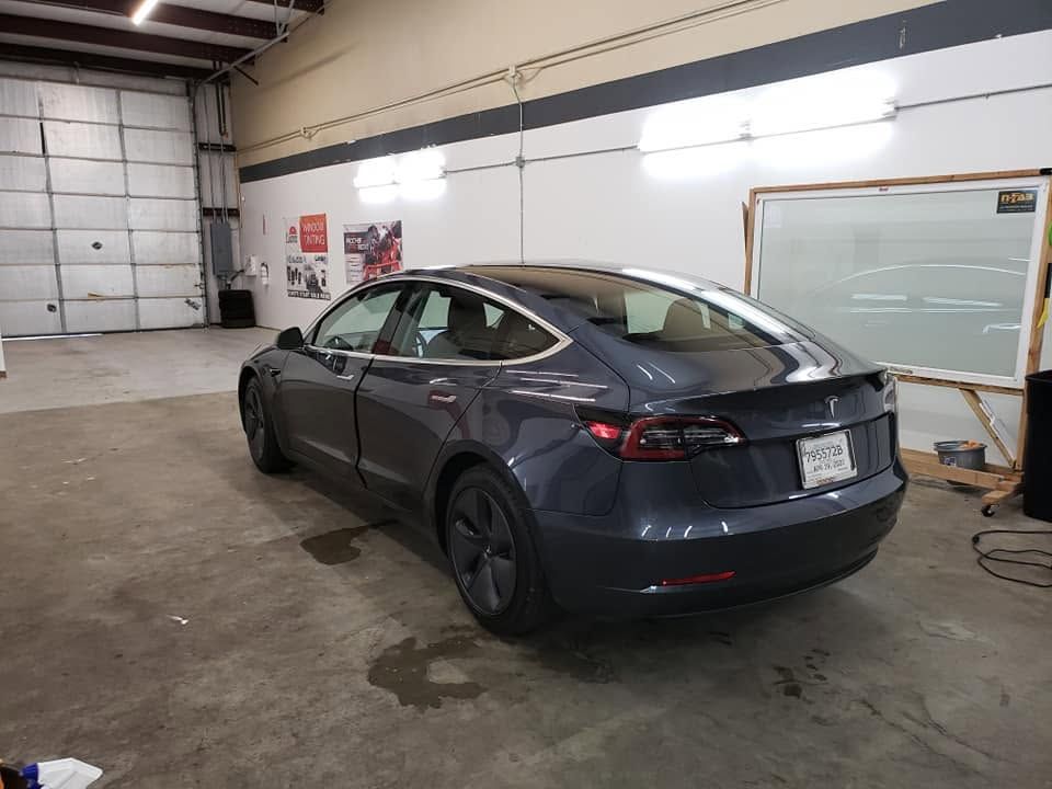 Dark gray sedan parked inside a garage with white walls and concrete floor.