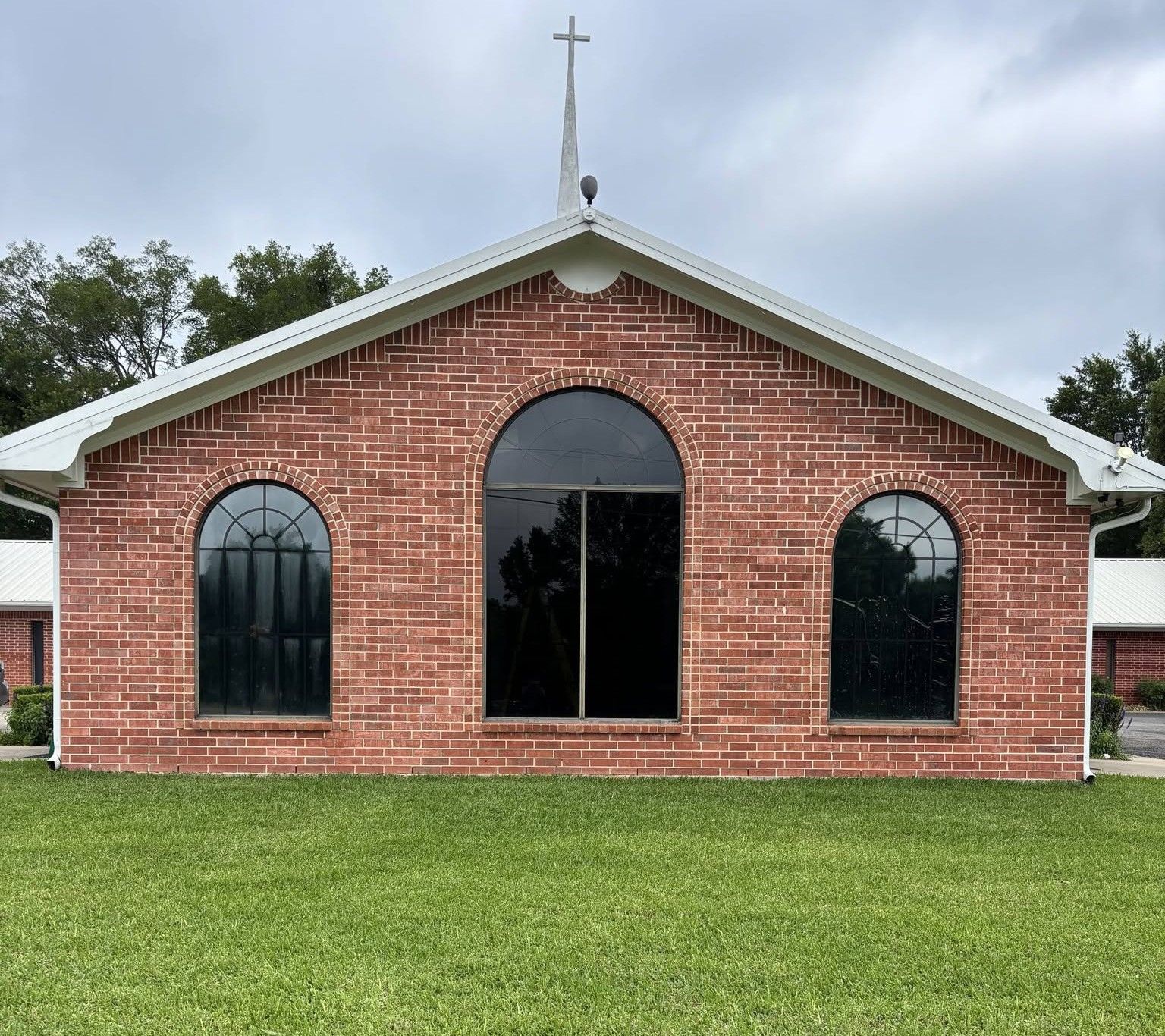 Red brick church with arched windows and a cross on the roof, fronted by a green lawn