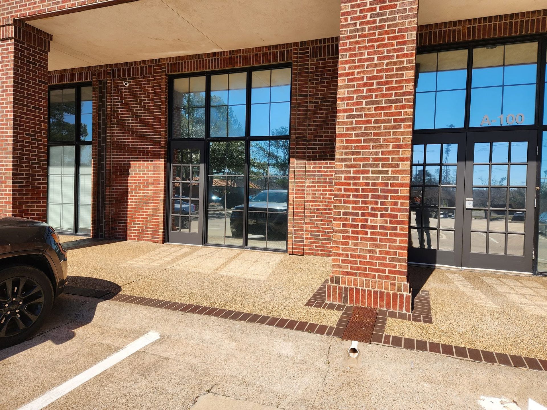 Brick storefront with large windows and parked car at the curb