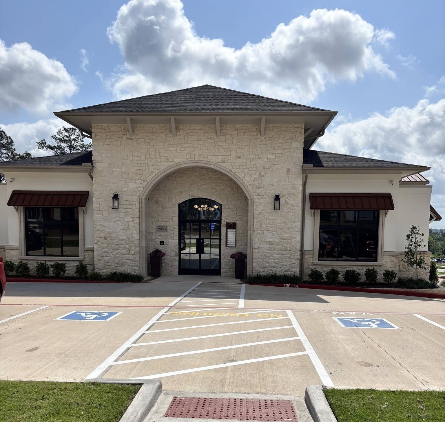 Front entrance of a cream stucco building with arched doorway and accessible parking spaces under a cloudy sky