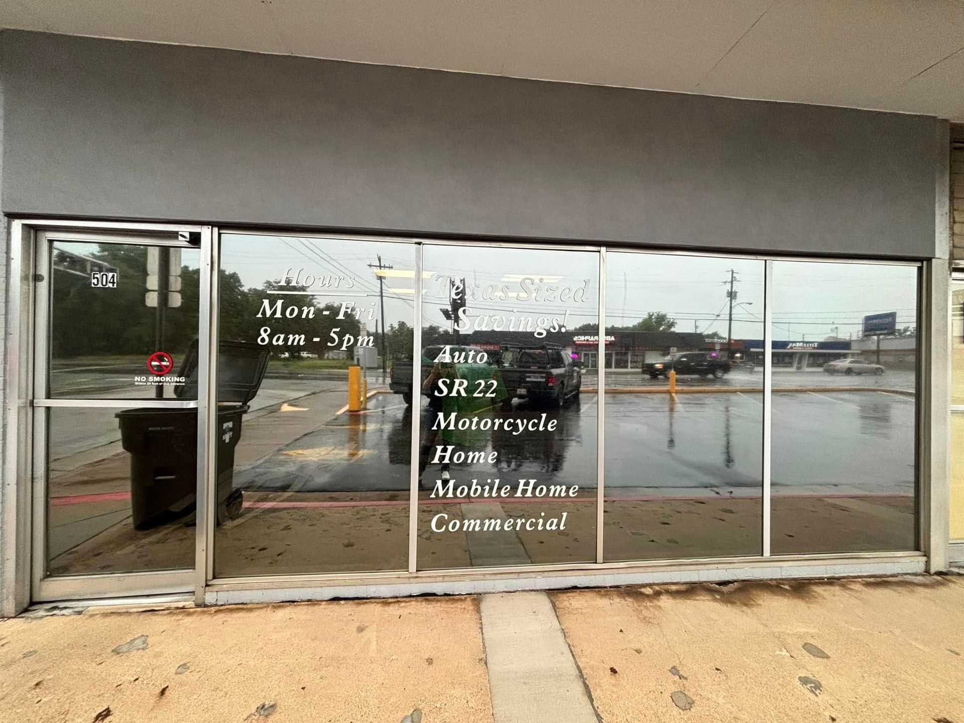 Storefront with glass doors and white lettering on a rainy parking lot street scene