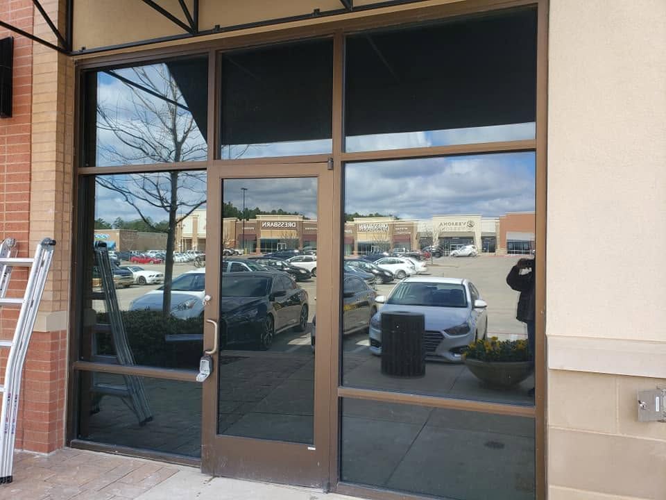 Glass storefront entrance with dark tinted doors reflecting a parking lot and nearby buildings