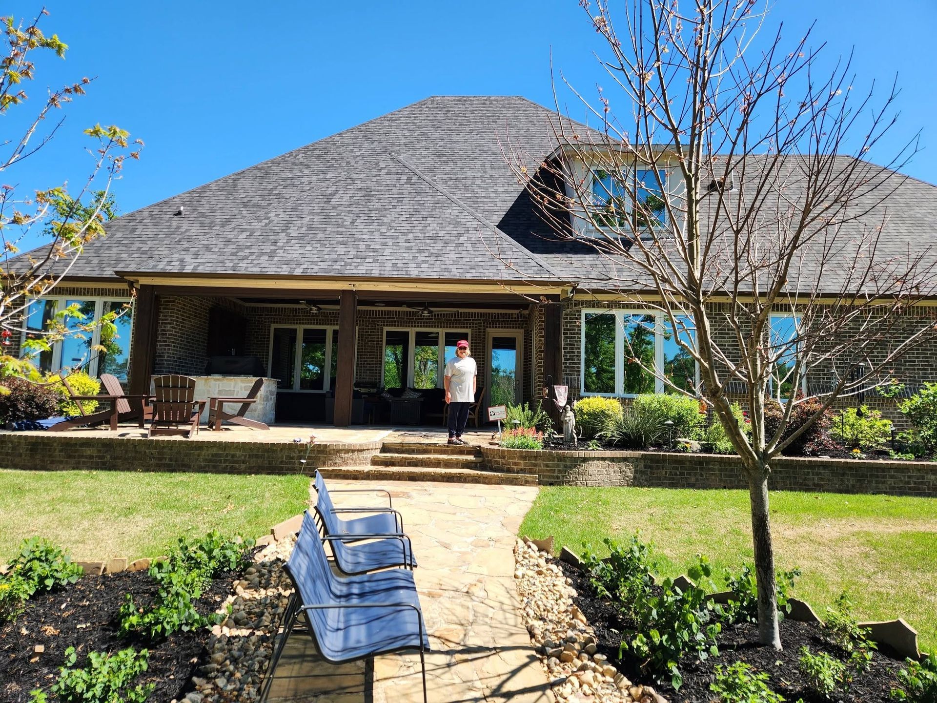 House with a front porch and landscaped yard, with a person standing near the entrance under a clear blue sky