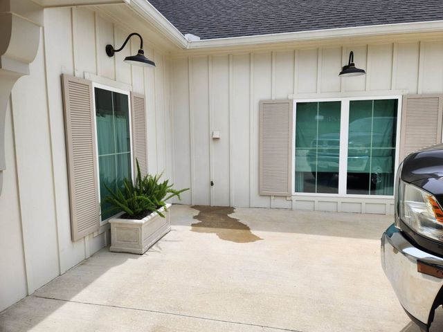 Front patio with cream siding, two windows, potted plant, and part of a parked car.