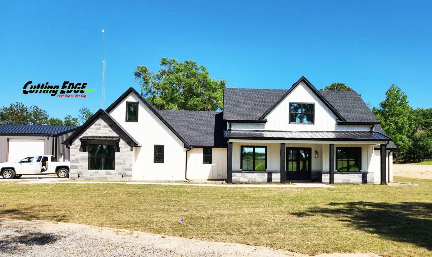 White house with black roof and porch on a grassy lot under a clear sky