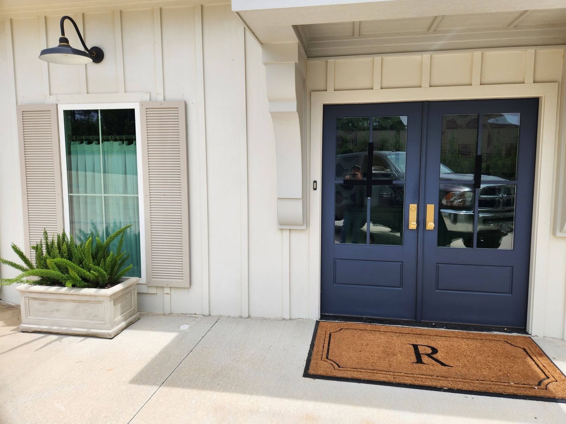 Blue double front doors with brass handles, a tan doormat, and a white planter beside shuttered window shutters.
