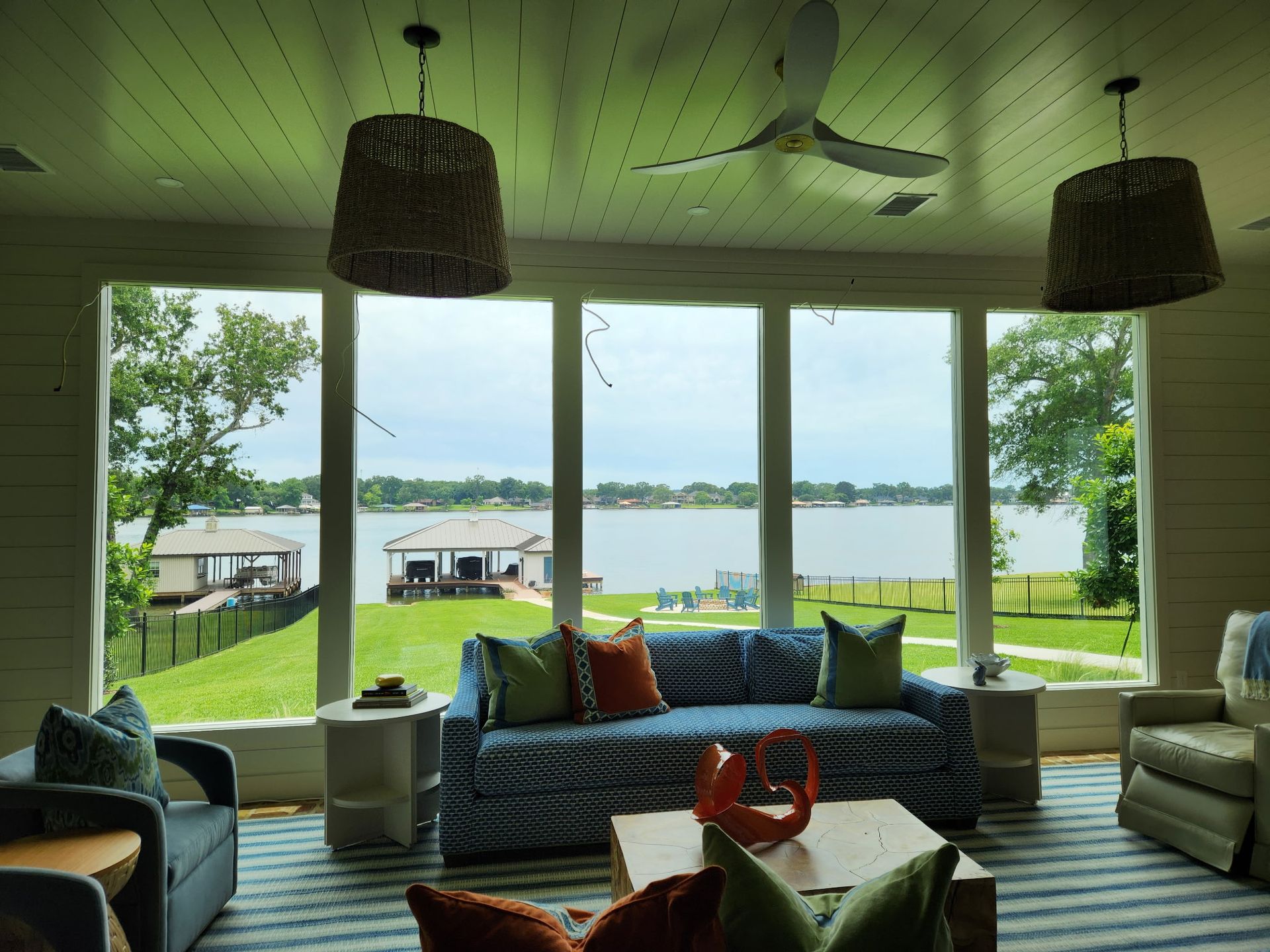 Lakefront porch with wicker seating, hanging lamps, and large windows overlooking water and boats