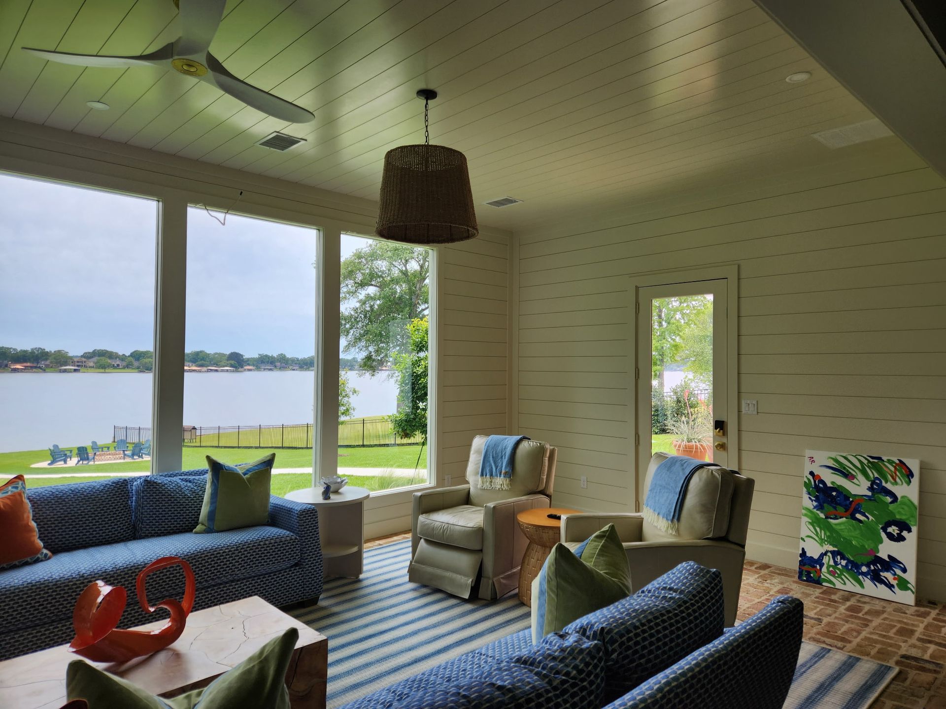 Lakefront living room with blue sofa, wicker chairs, and large windows overlooking water