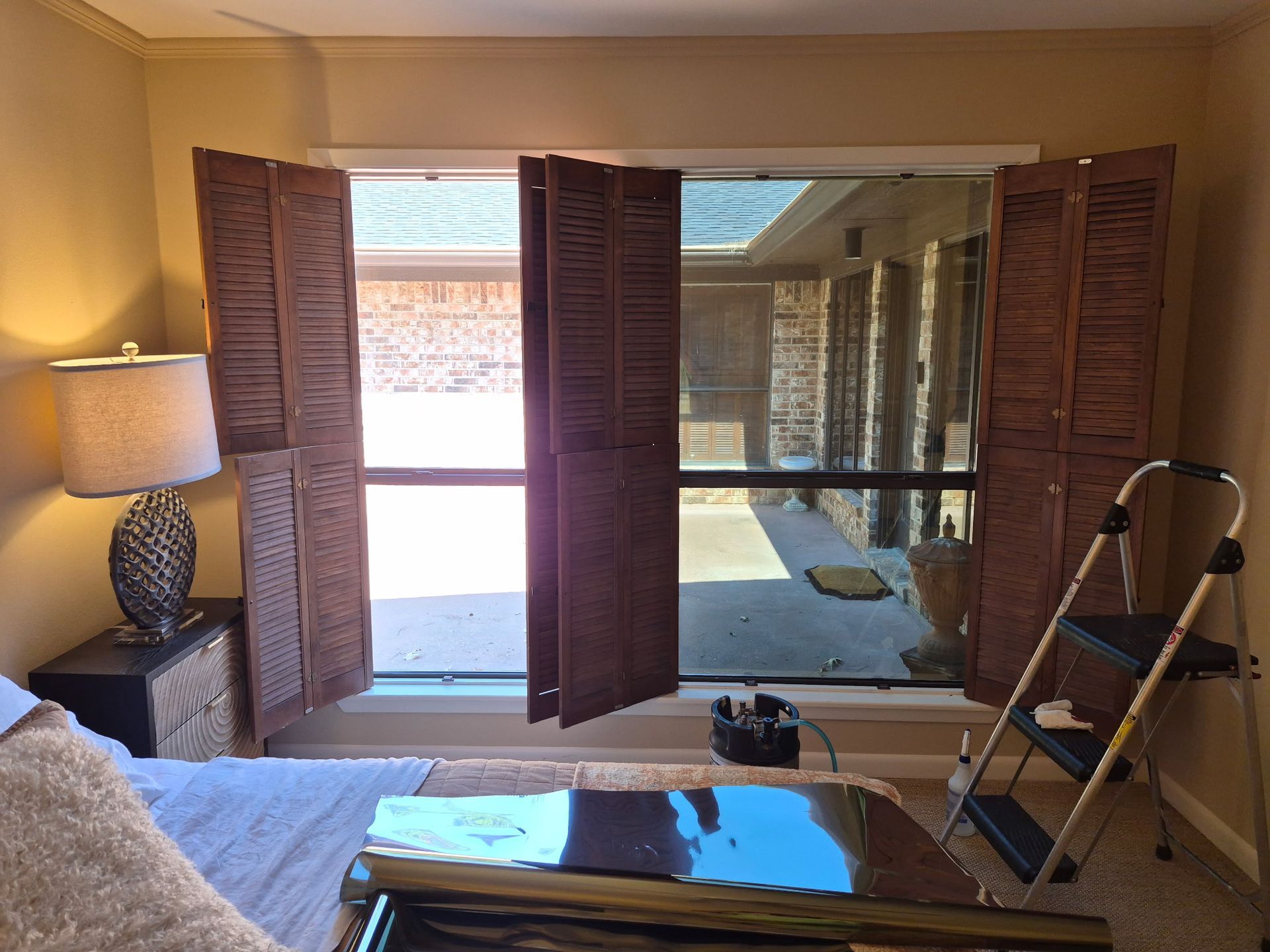 Living room with open shutters, lamp, sofa, and a step ladder beside a mirrored wall