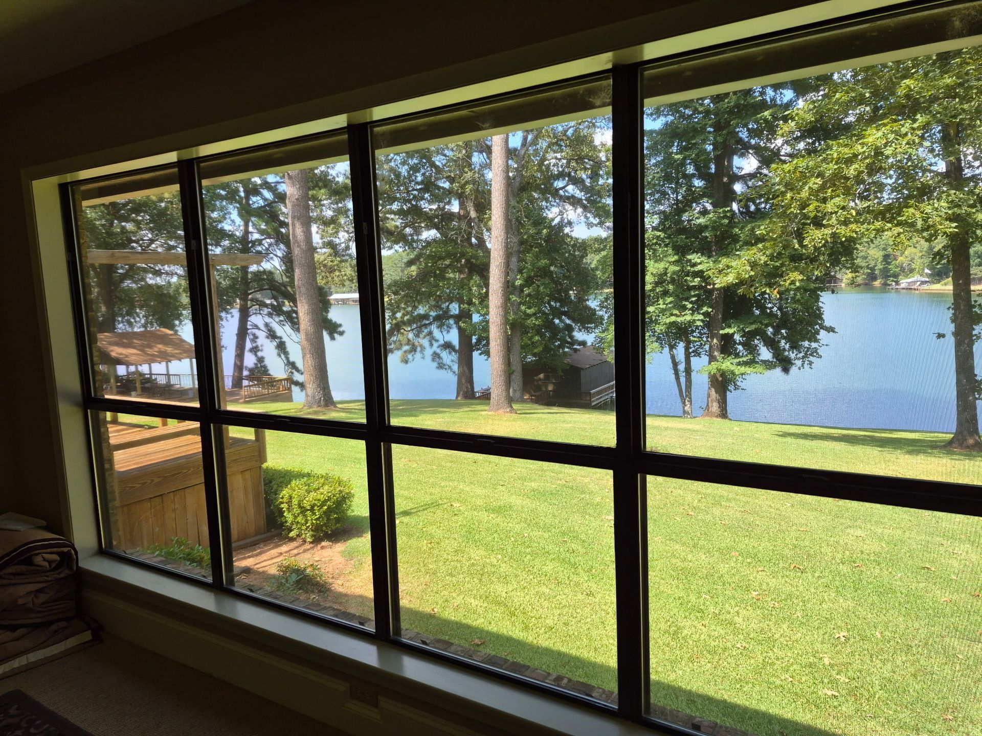 Living room window overlooking a green lawn and lake with trees outside