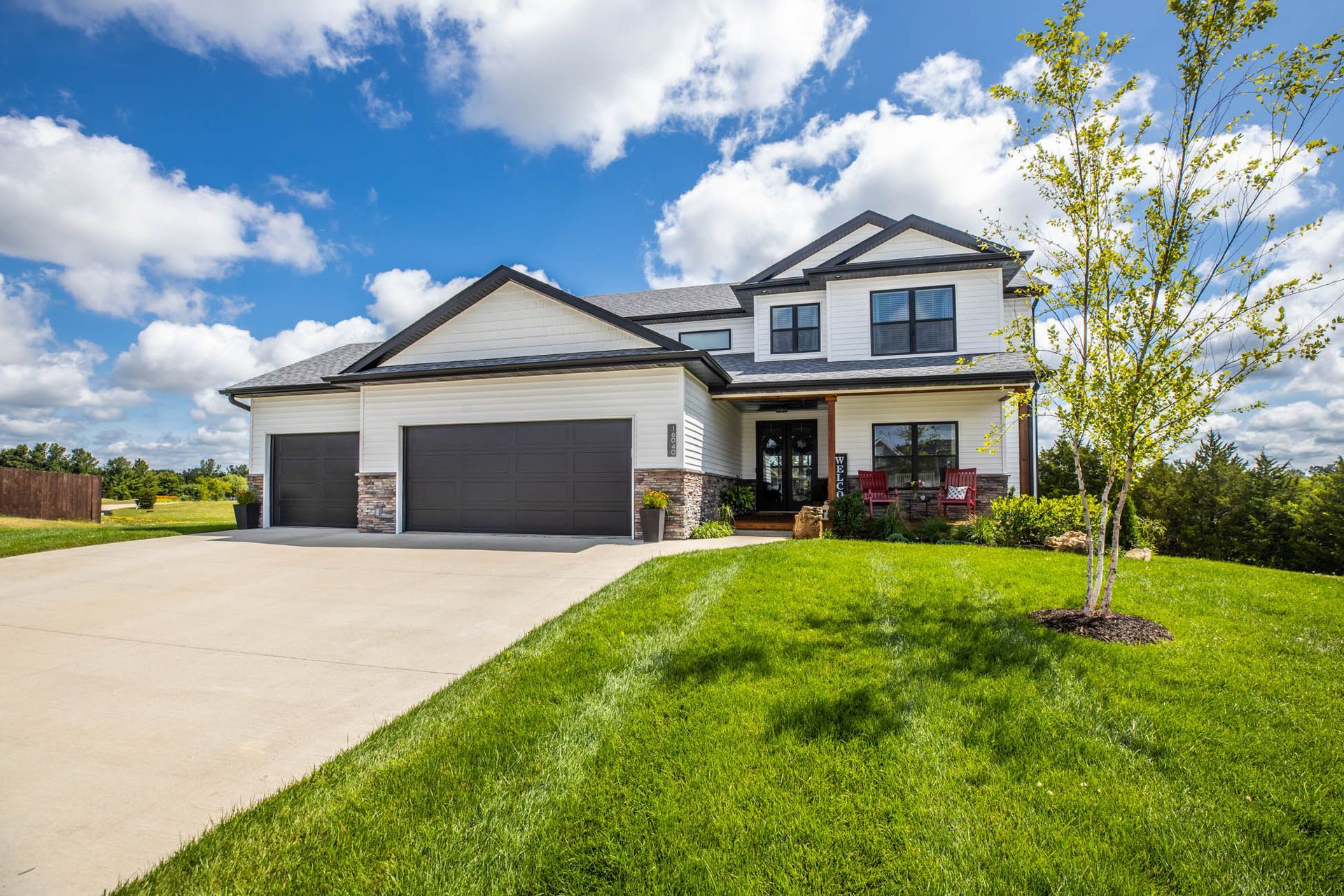 A large white house with a black garage door is sitting on top of a lush green hill