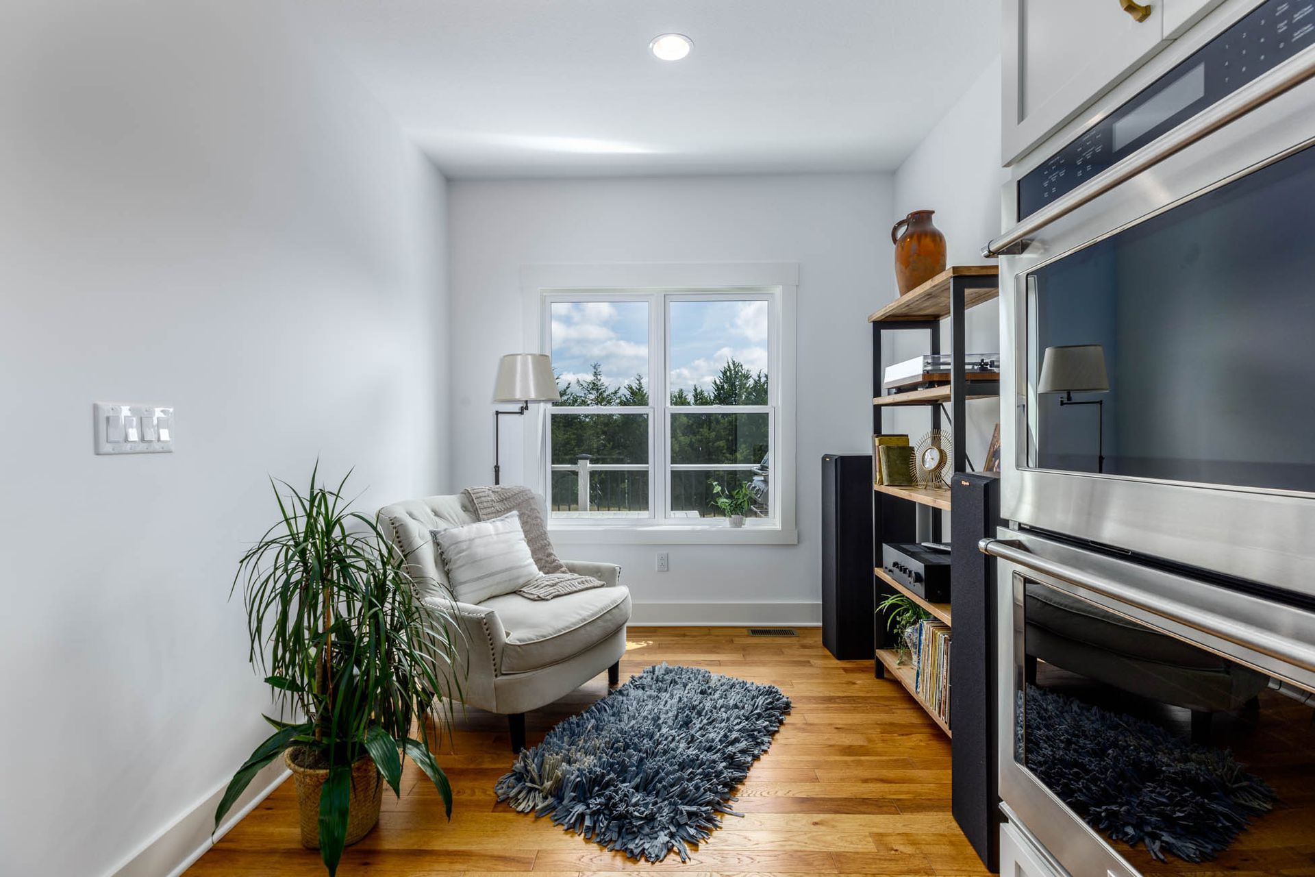 A living room with a chair, rug, ovens, and a window