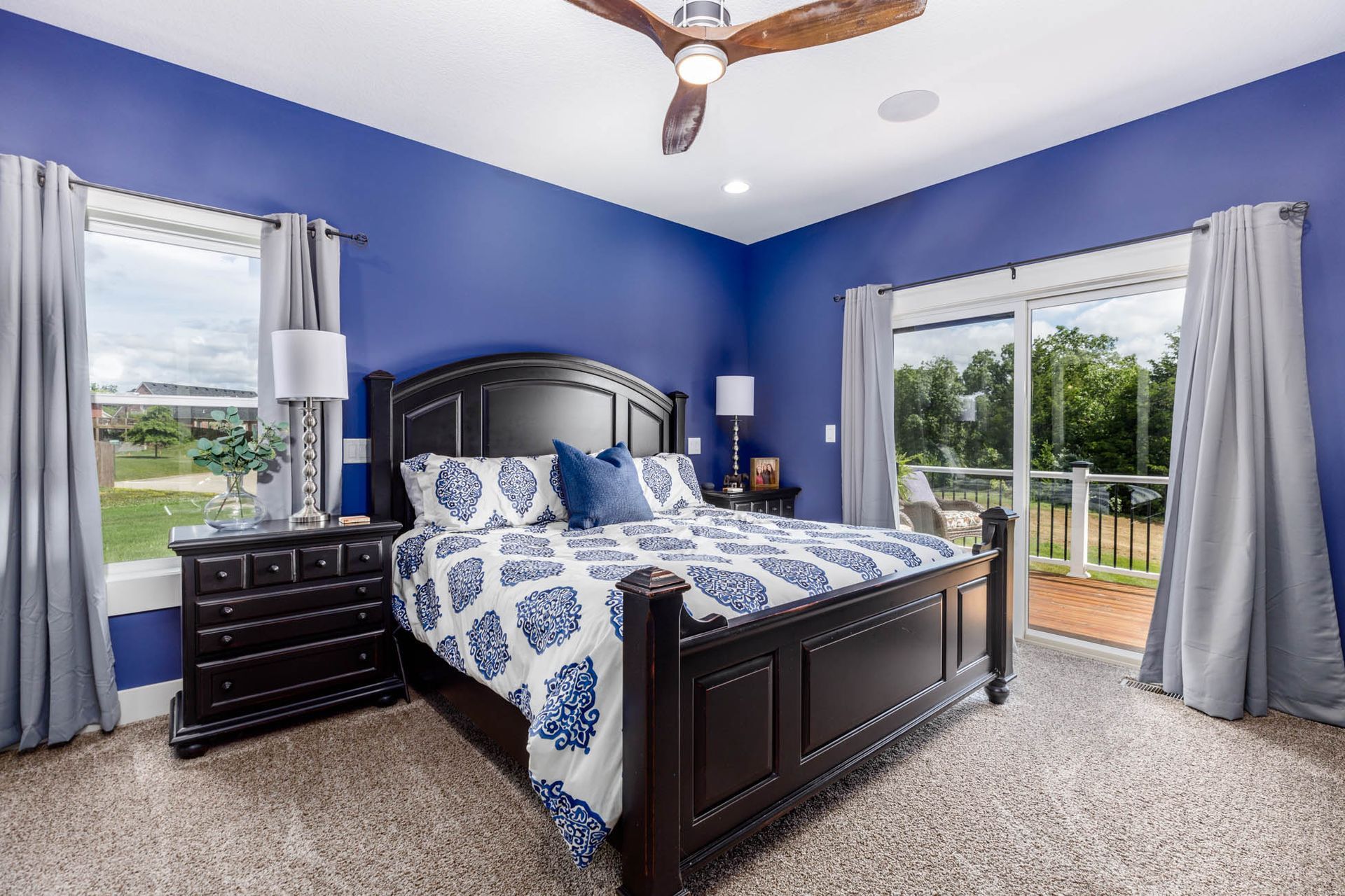A bedroom with blue walls, a king size bed, a nightstand, and a ceiling fan