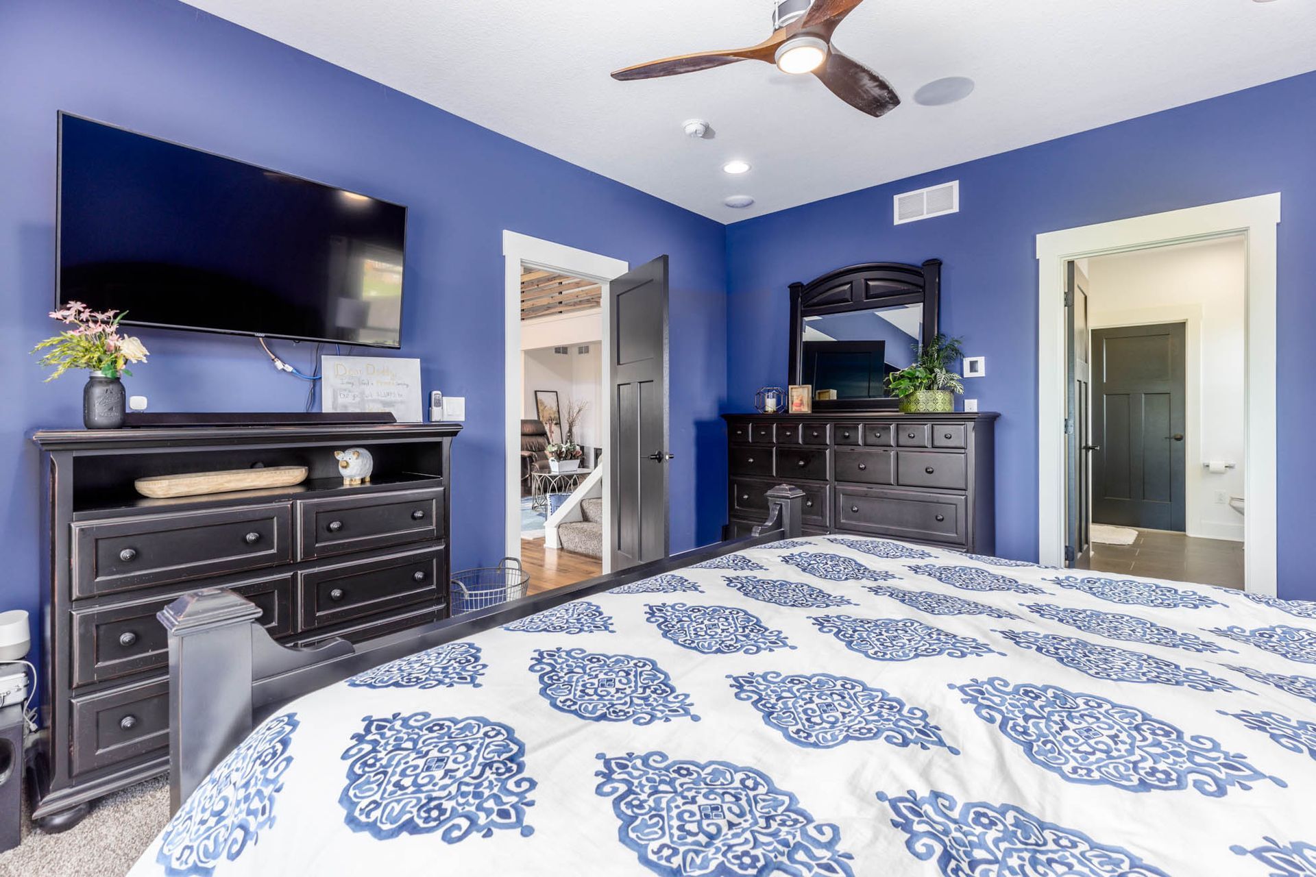 A bedroom with a bed, dresser, television, and ceiling fan