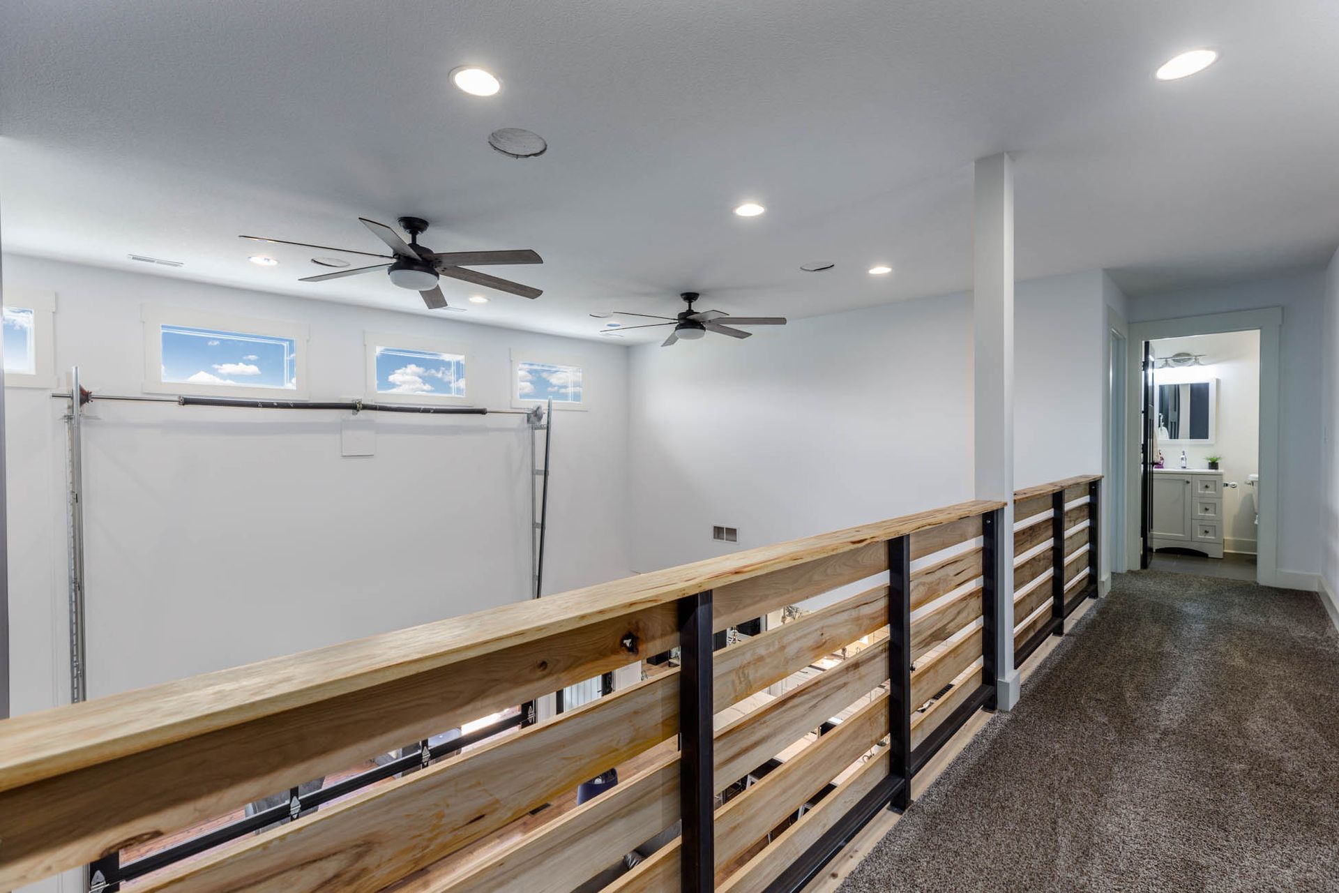A hallway with a wooden railing and ceiling fans in a house