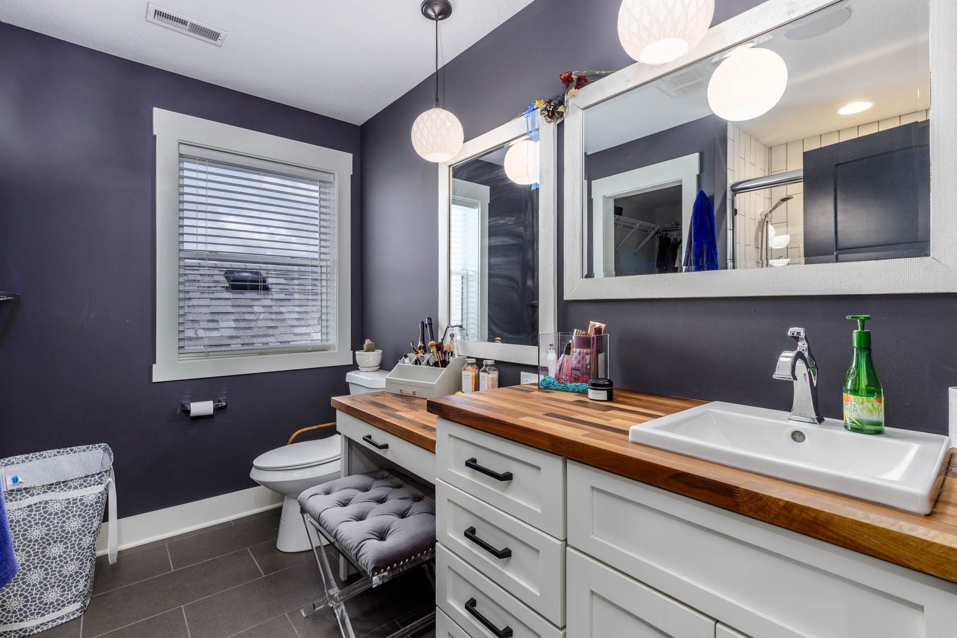 A bathroom with two sinks, two mirrors, a toilet, and a window