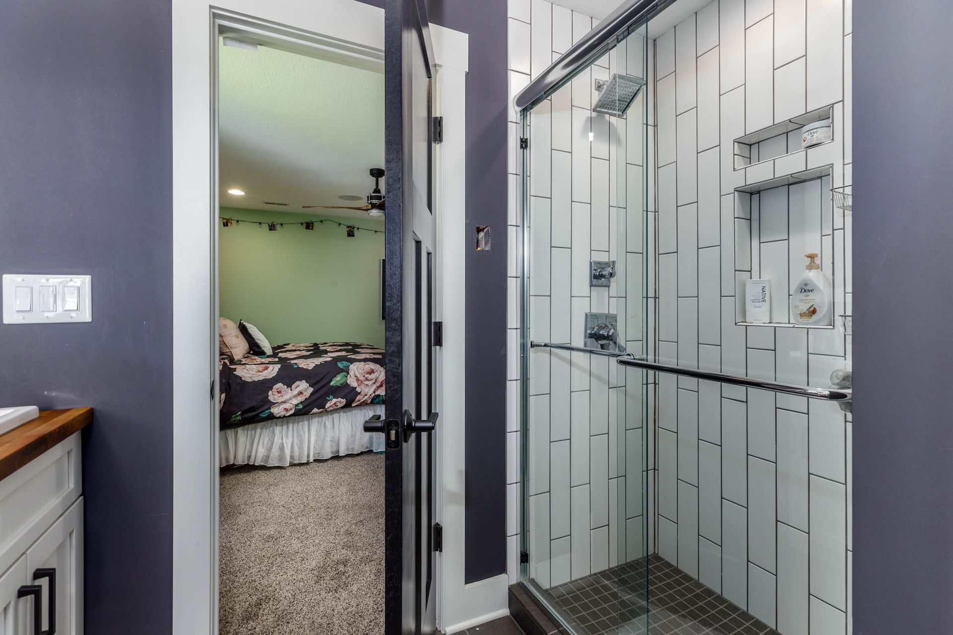 A bathroom with a walk in shower and a glass door leading to a bedroom