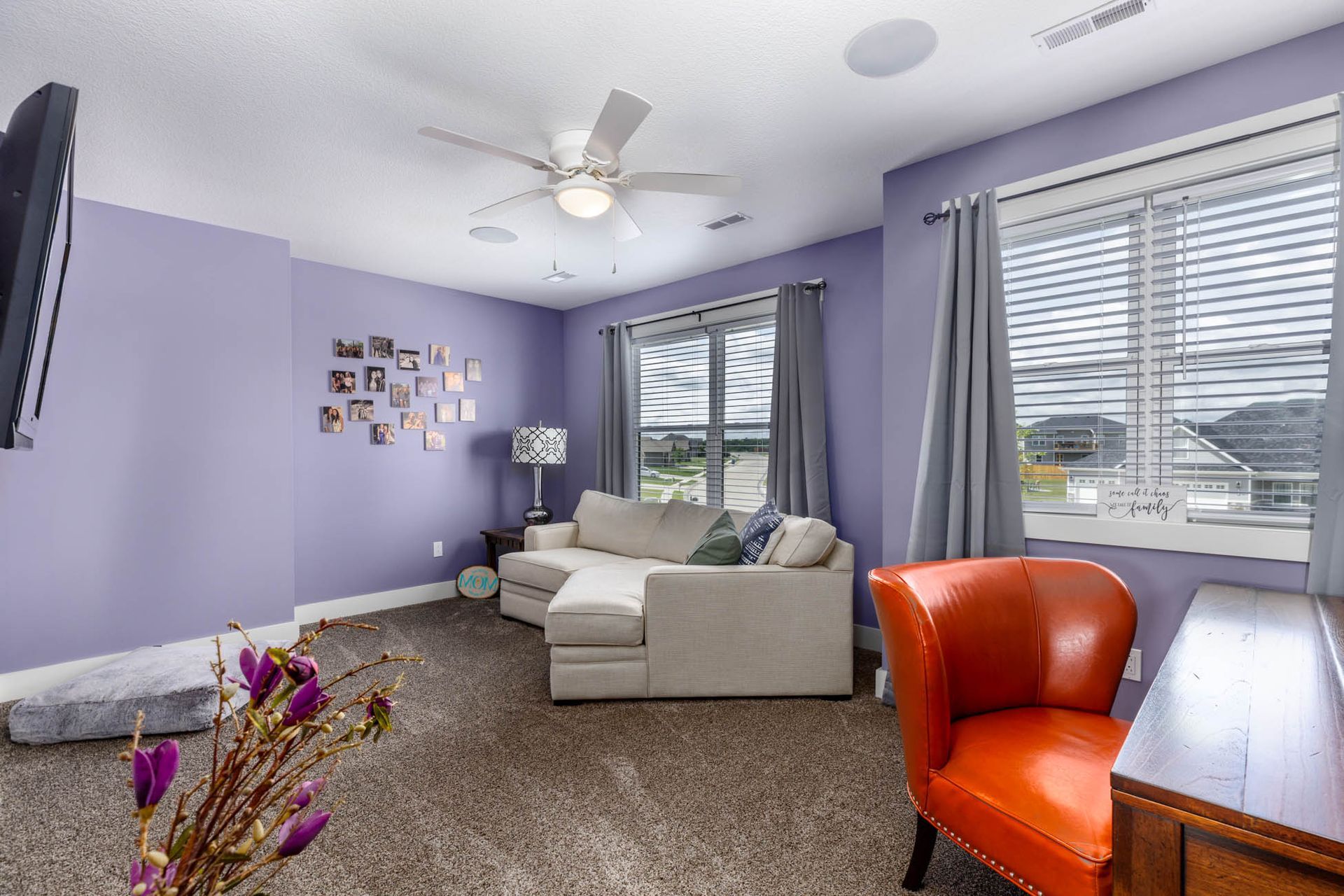 A living room with purple walls , a sectional couch, an orange chair, and a ceiling fan