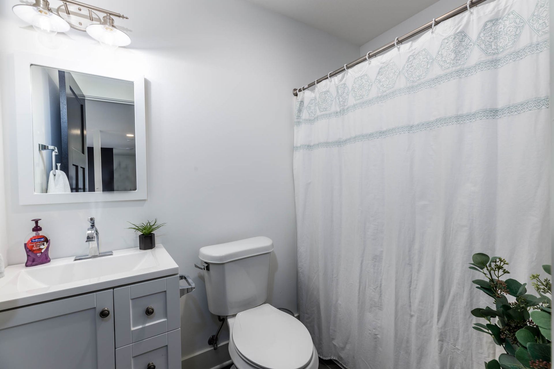A bathroom with a toilet, sink, mirror, and shower curtain