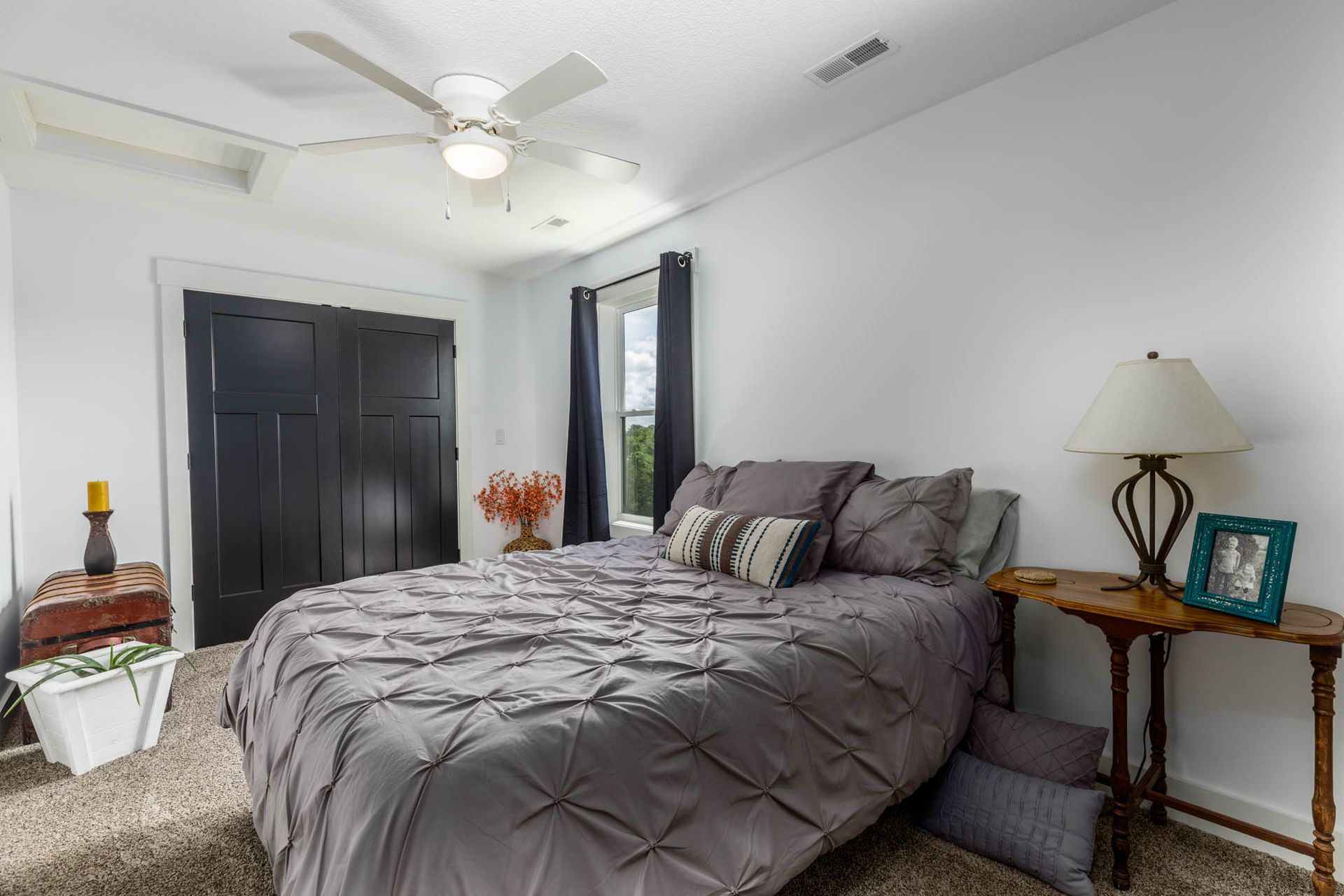 A bedroom with a bed, nightstand, lamp, and ceiling fan