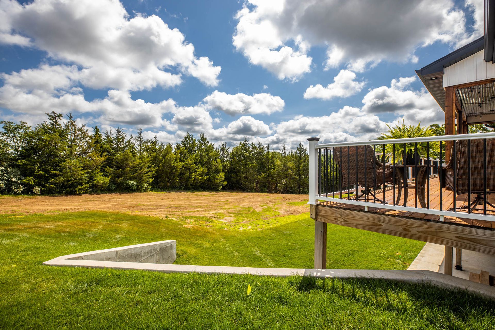 A large lawn with a deck in the background and a house in the background