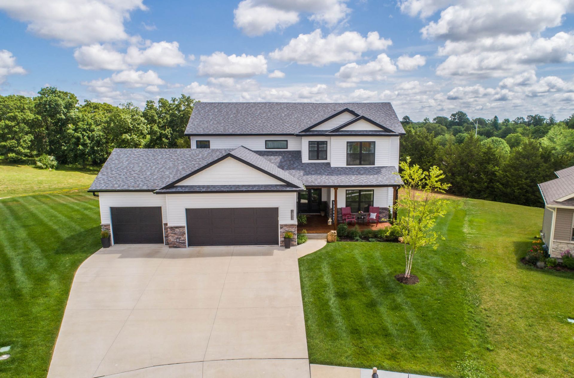 An aerial view of a large house with a lush green yard and a driveway