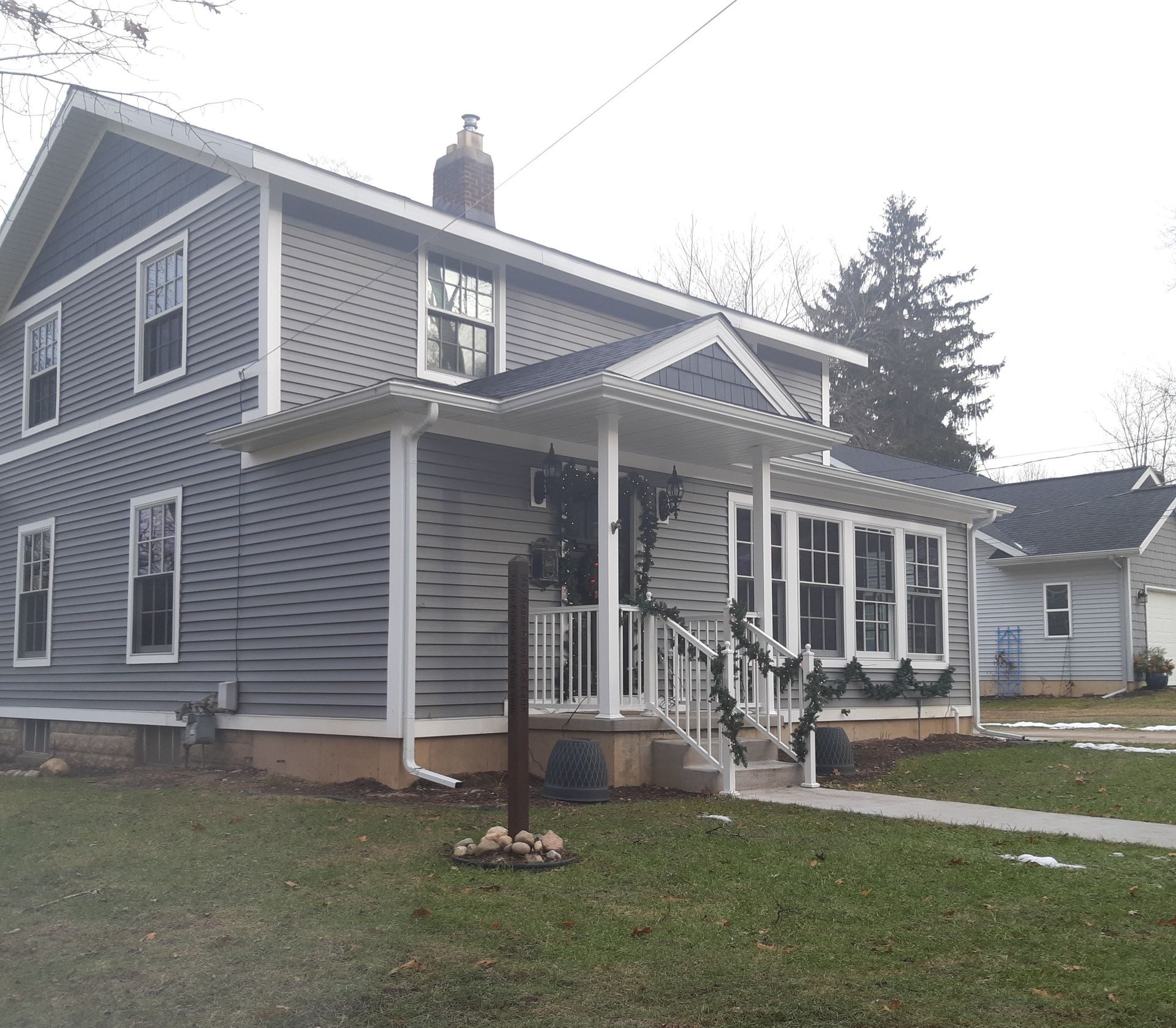 Gray two-story house with white trim and a small front porch on a grassy lawn.
