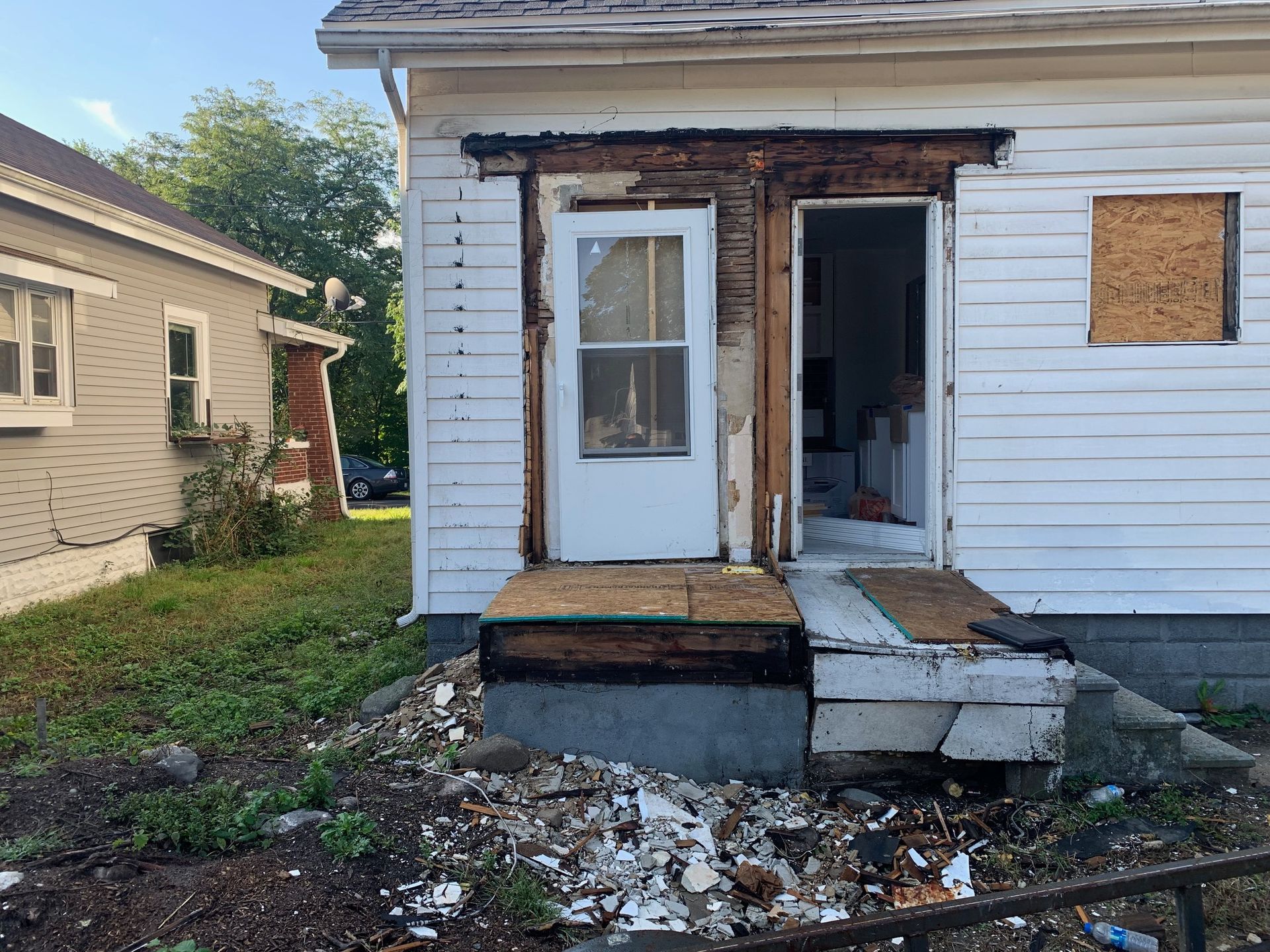 Partially demolished house entry with broken steps, exposed framing, and debris in the yard