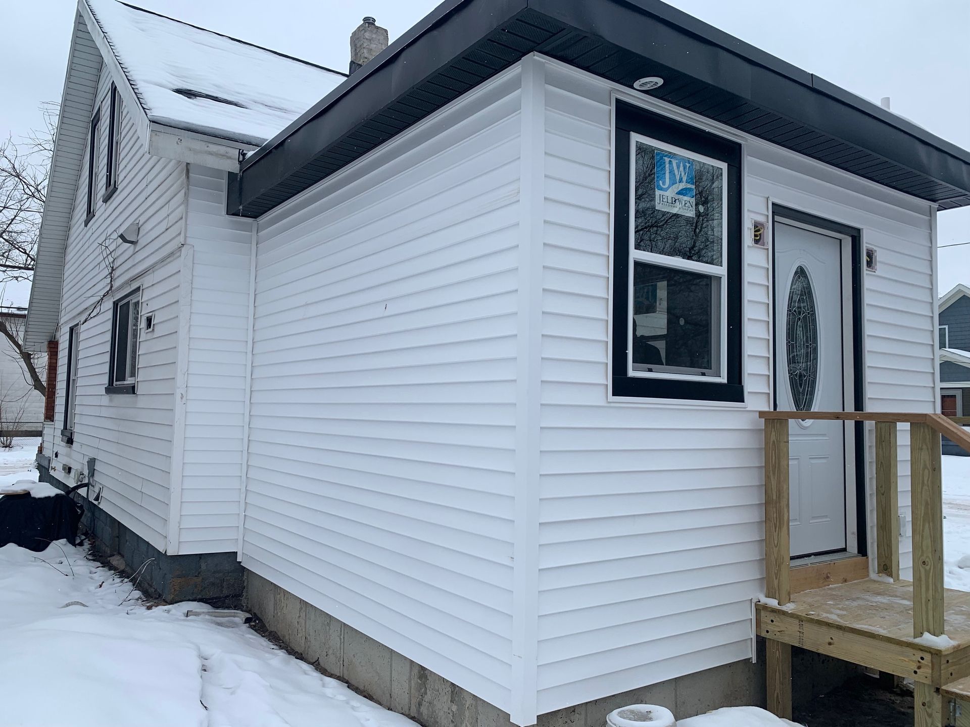 Snow-covered white house with black trim and a small wooden front porch.