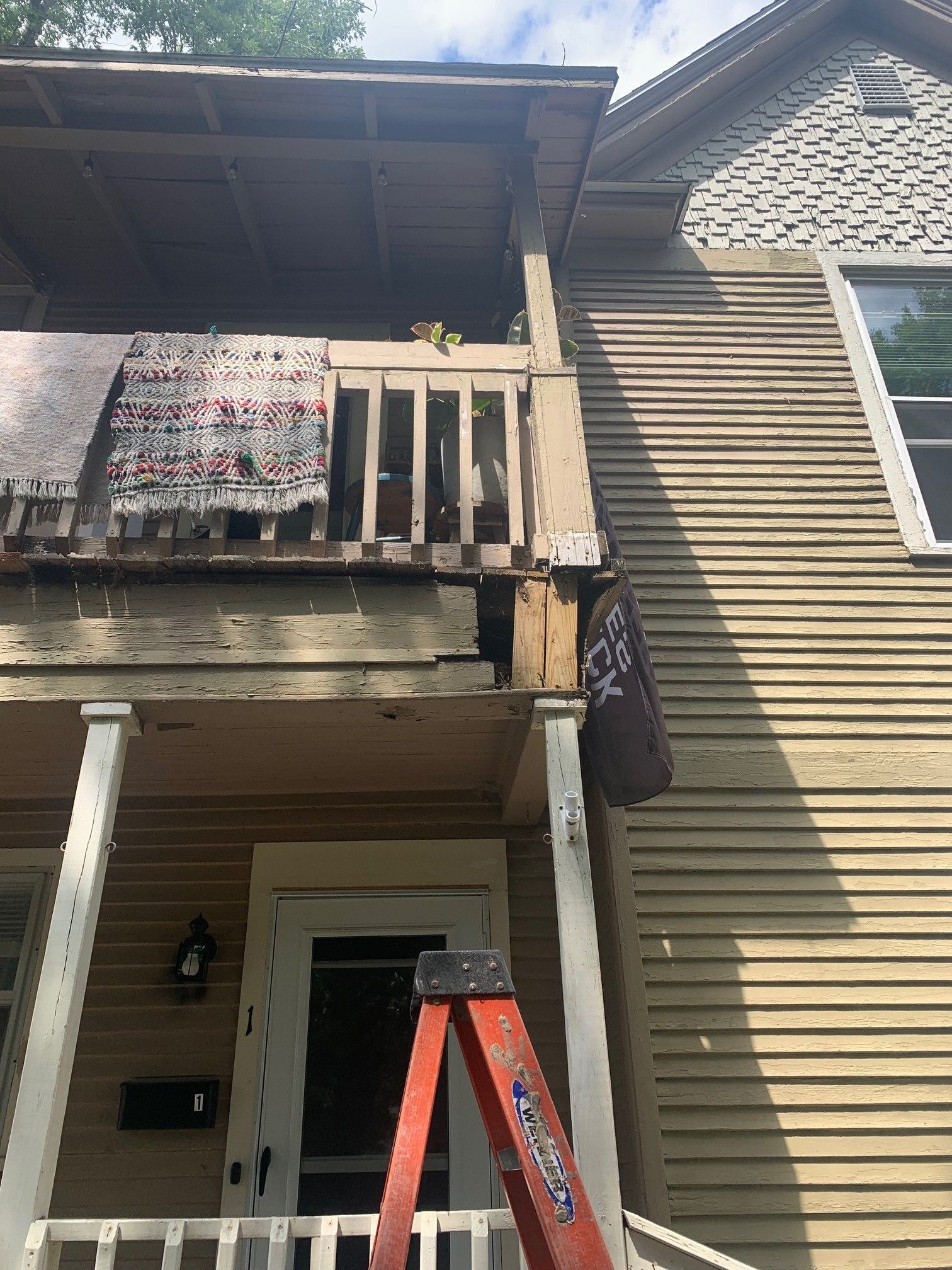 Damaged apartment balcony with broken railing and a red ladder leaning against the building