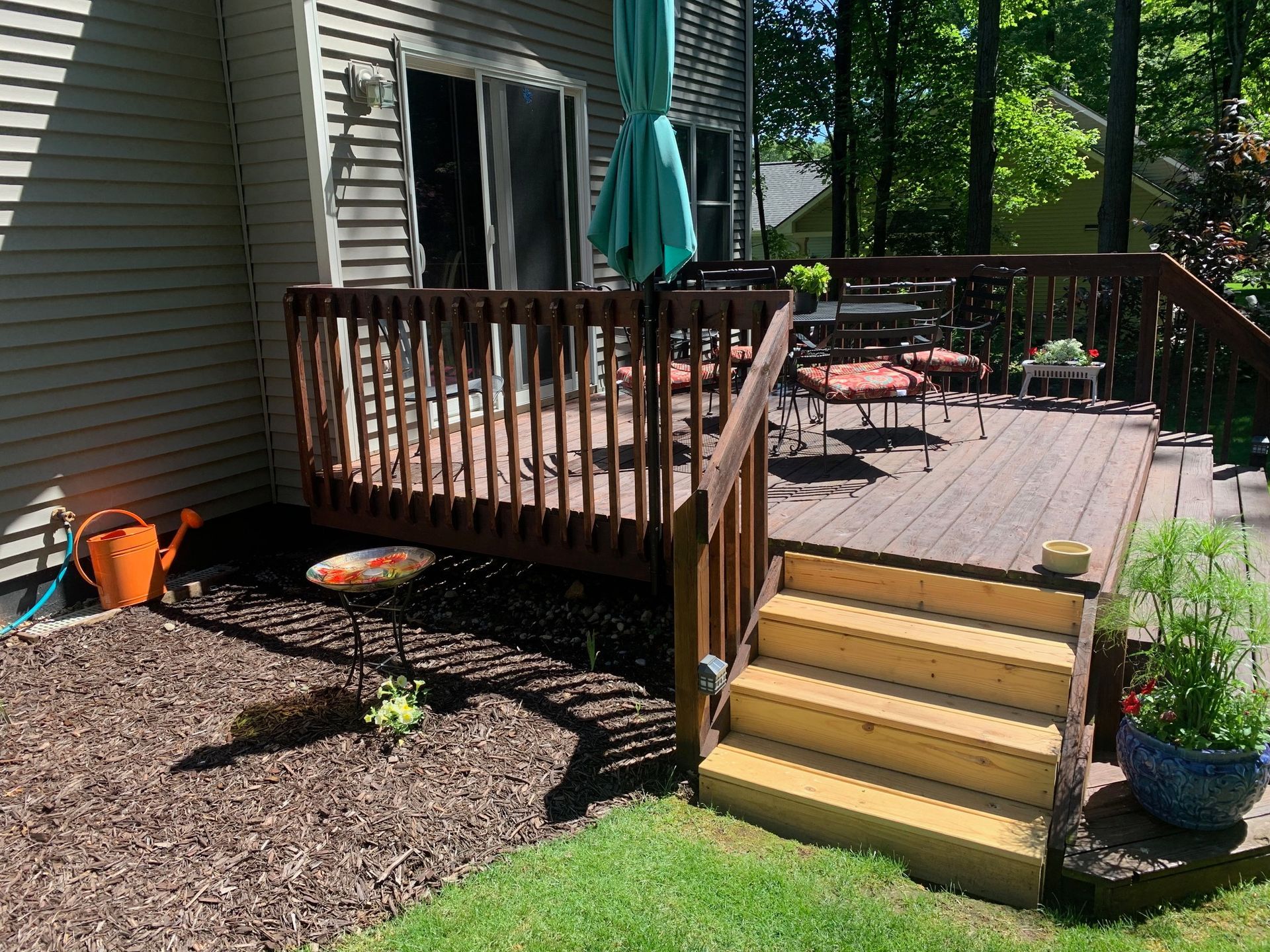 Backyard deck with wooden stairs, railing, potted plants, and patio furniture beside a house