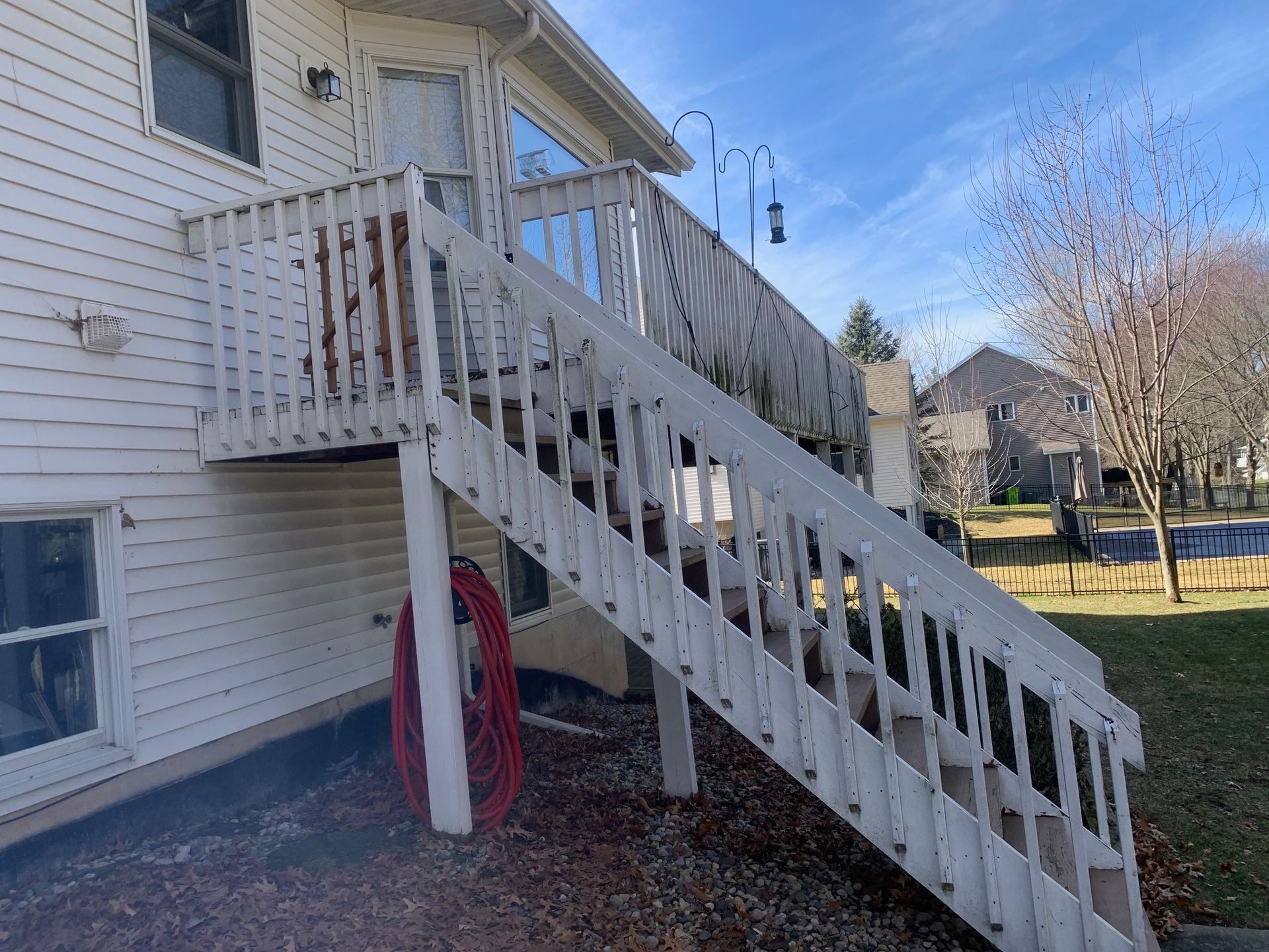 Wooden exterior staircase on a white house, with a yard and blue sky in the background.