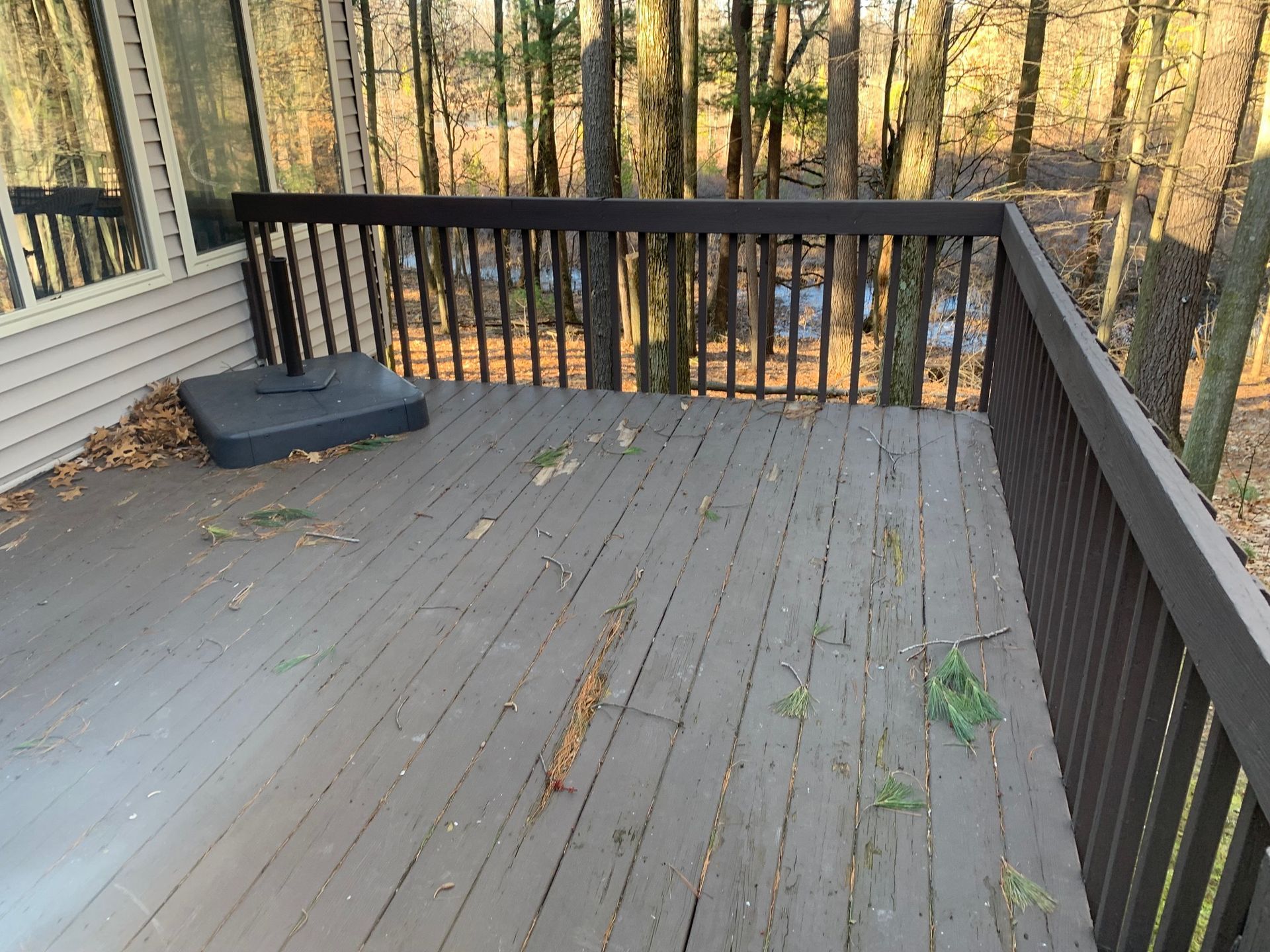 Empty wooden deck with gray floorboards, black railing, and a covered object near the house wall.