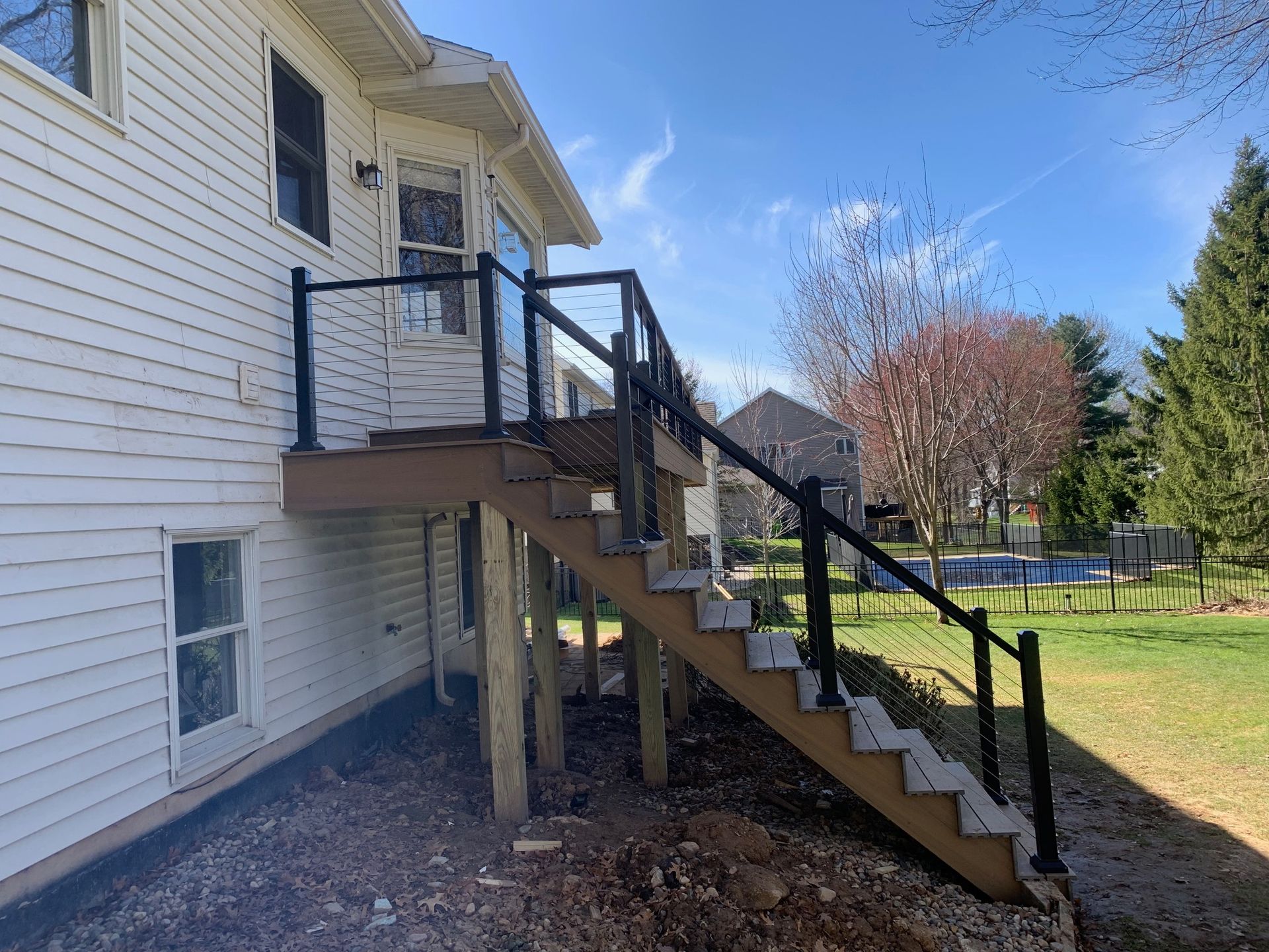Exterior wooden stairs with black railings attached to a white house, leading to a second-floor entrance.