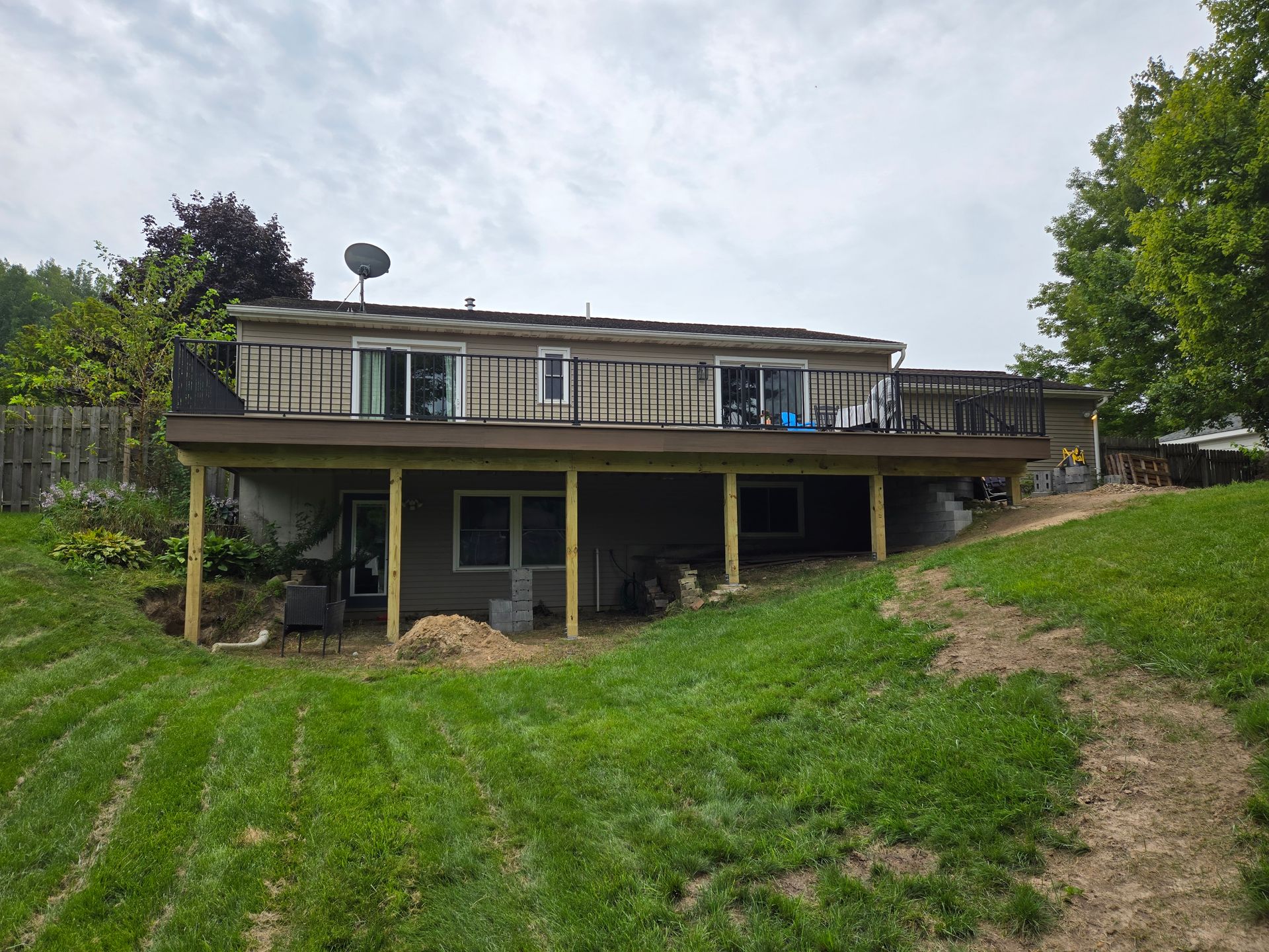 A house with a raised deck on a grassy hillside, viewed from the backyard.