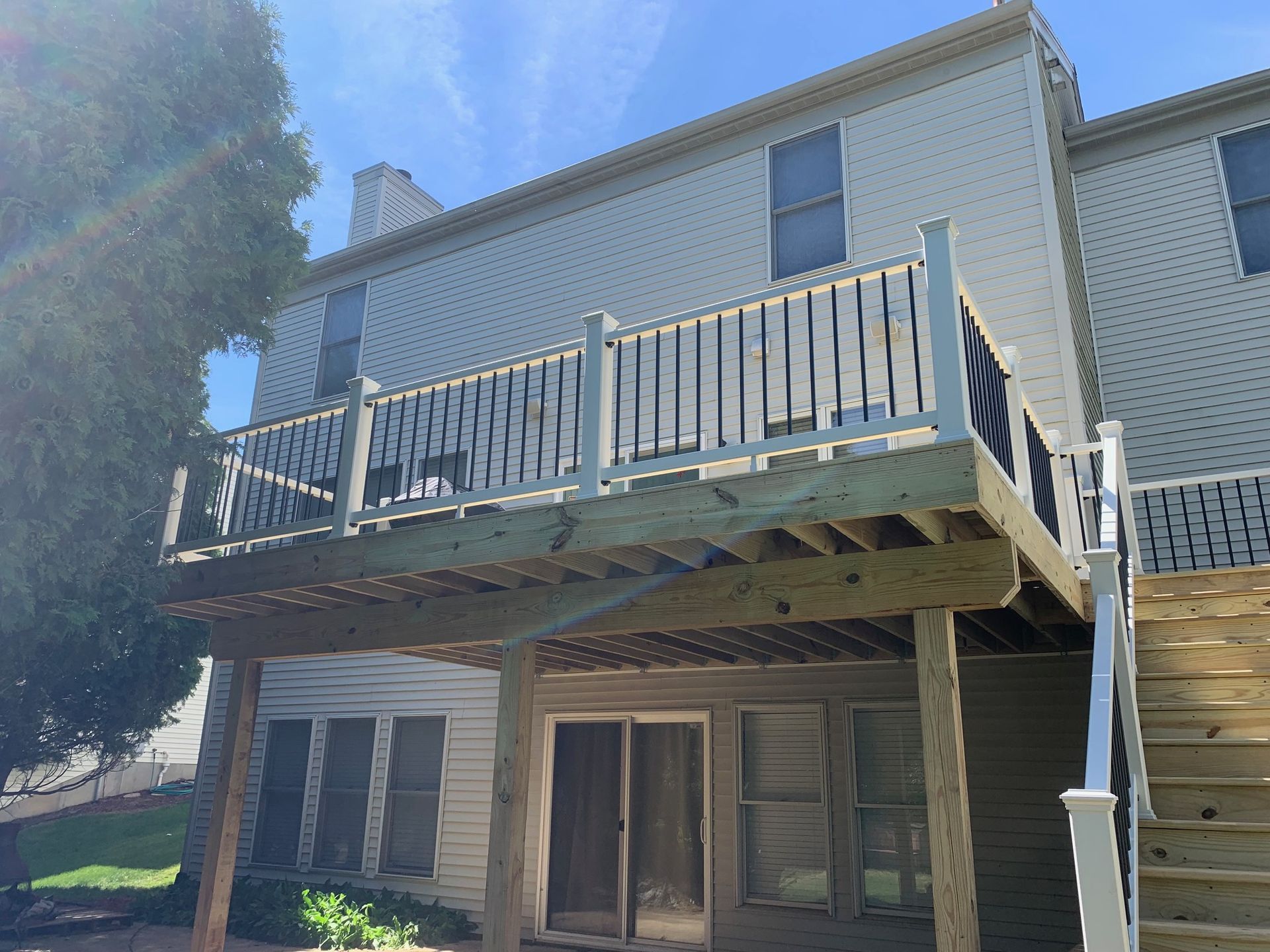 Two-story house with a raised wooden deck and stairs, viewed from below in daylight