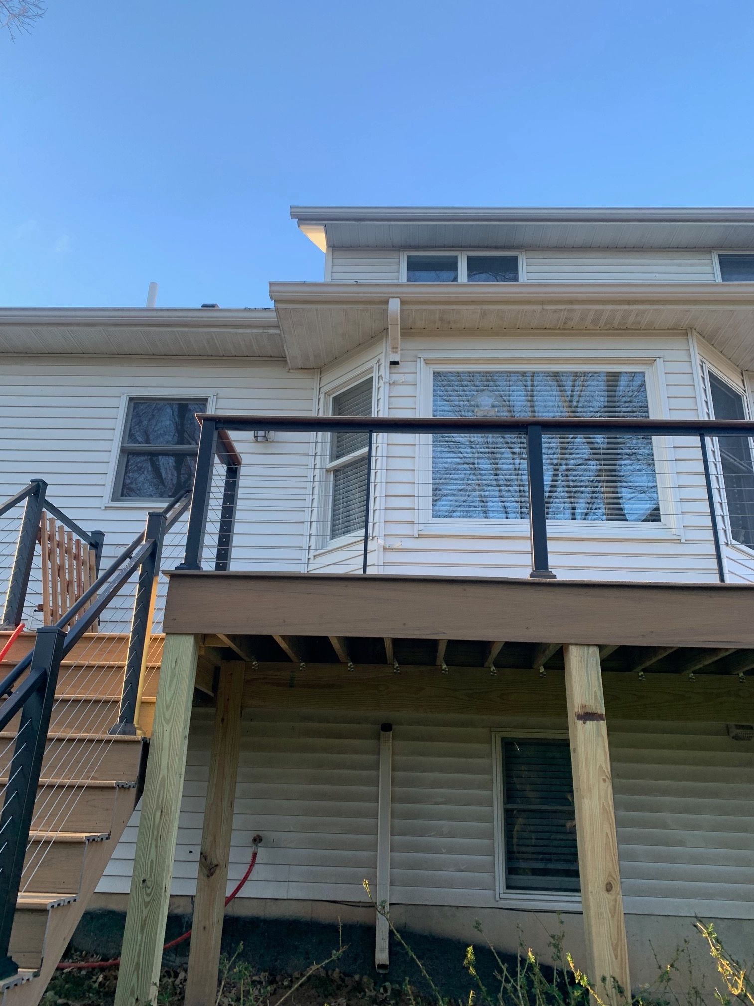 Back deck and stairs on a white house with black railing under a blue sky