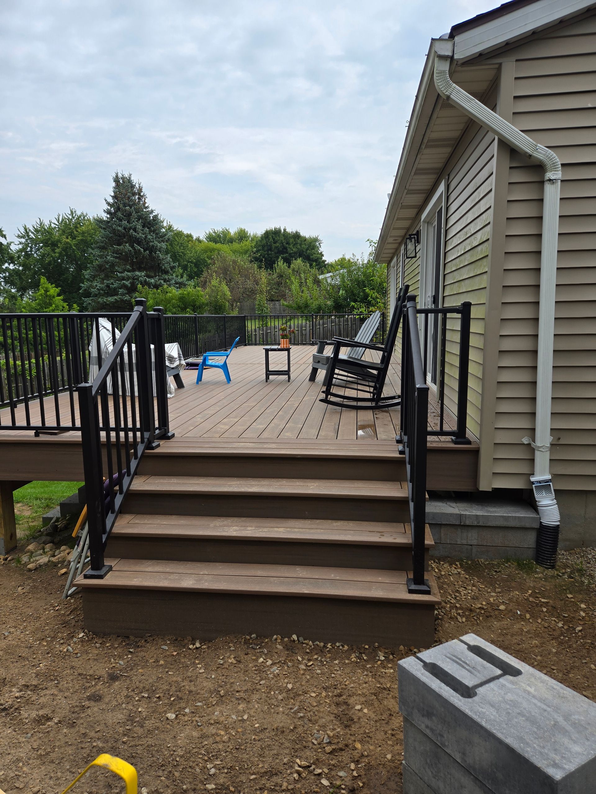 Back deck with stairs, black railings, and patio chairs beside a house
