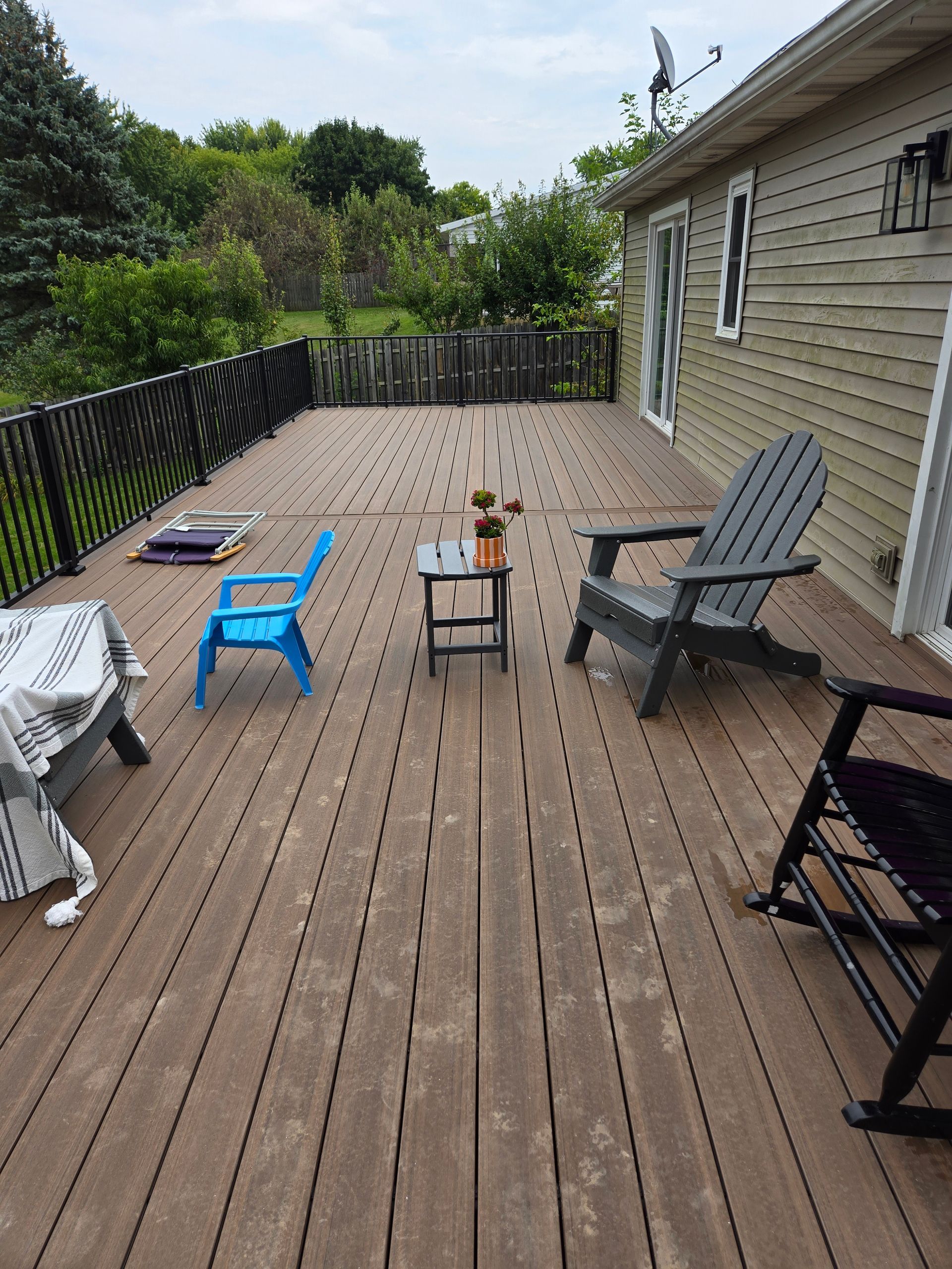 Wooden deck with patio chairs and small tables beside a house, overlooking trees and greenery