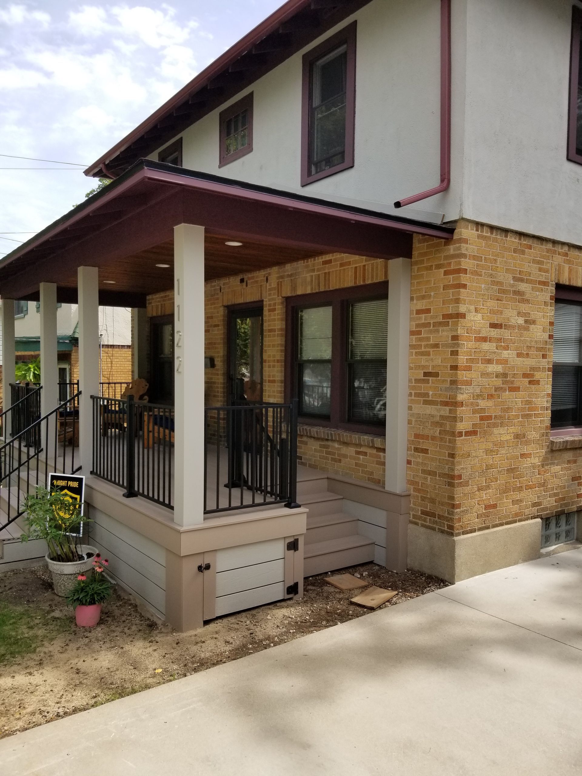 Covered front porch with beige columns, stone siding, and a red roof on a house.