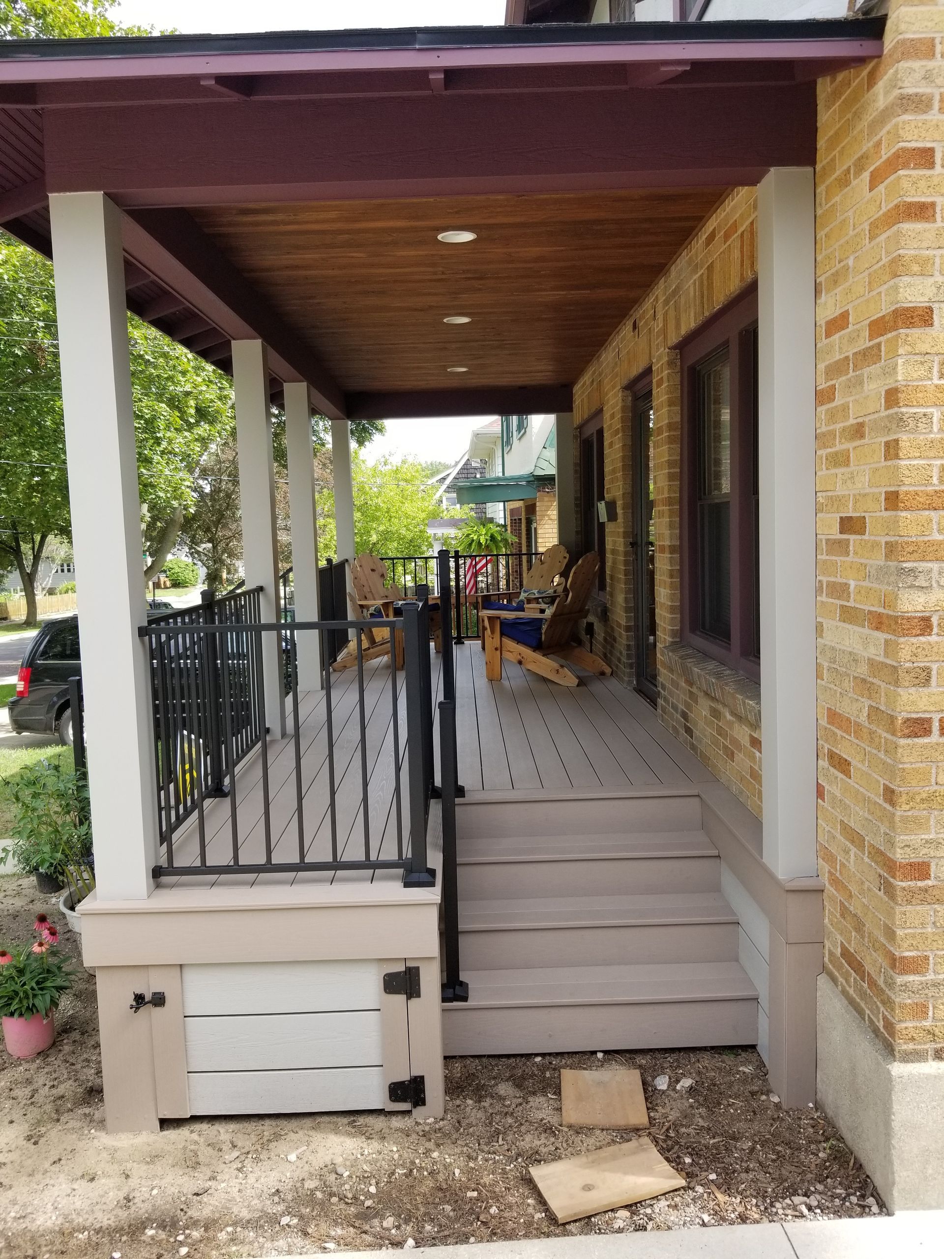 Front porch with steps, black railing, brick exterior, and a covered walkway beside the house.