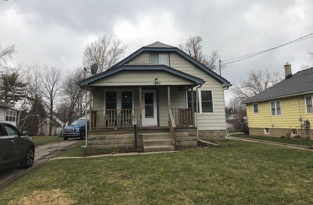 Small gray house with a front porch and steps, set on a grassy lot with neighboring homes.