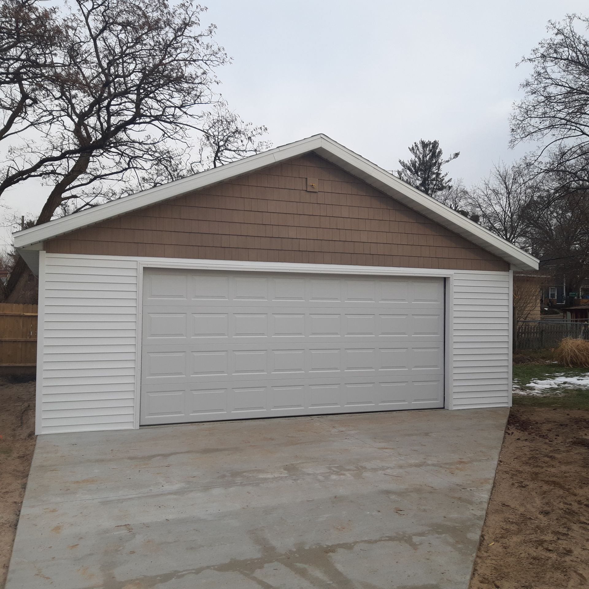 Detached two-car garage with white door and tan siding at the end of a concrete driveway