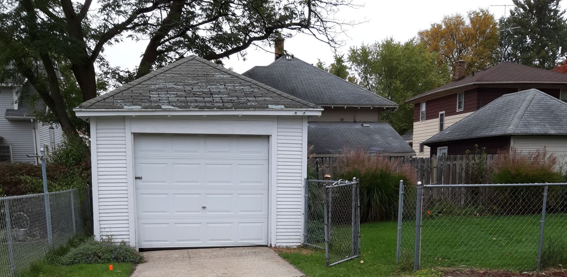 White detached garage with a closed door beside a chain-link fence in a residential yard.
