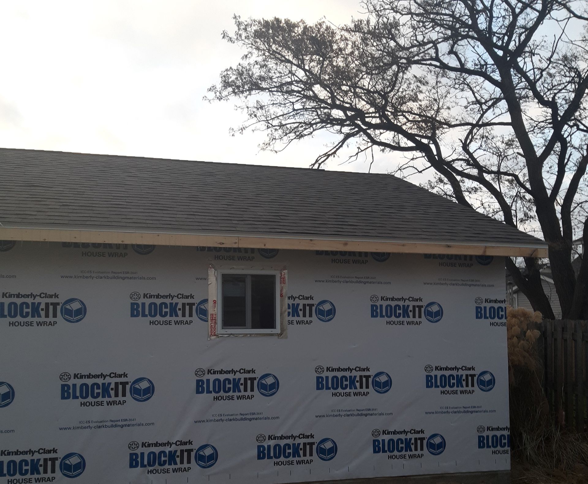 Partially renovated house wrapped in BOCIT house wrap, with a window and leafless tree beside it