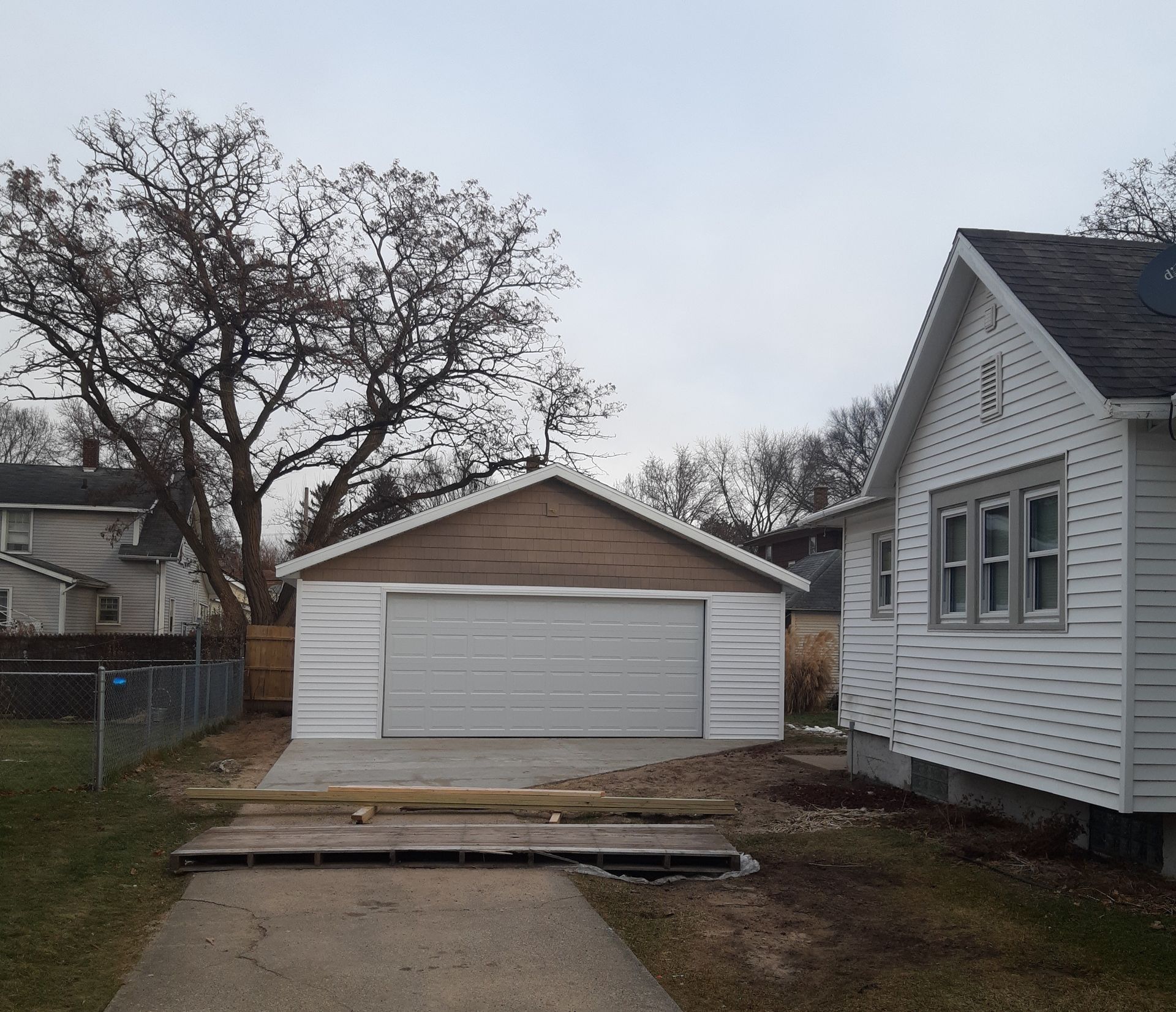 White detached garage with closed door behind a concrete driveway, framed by houses and bare trees.