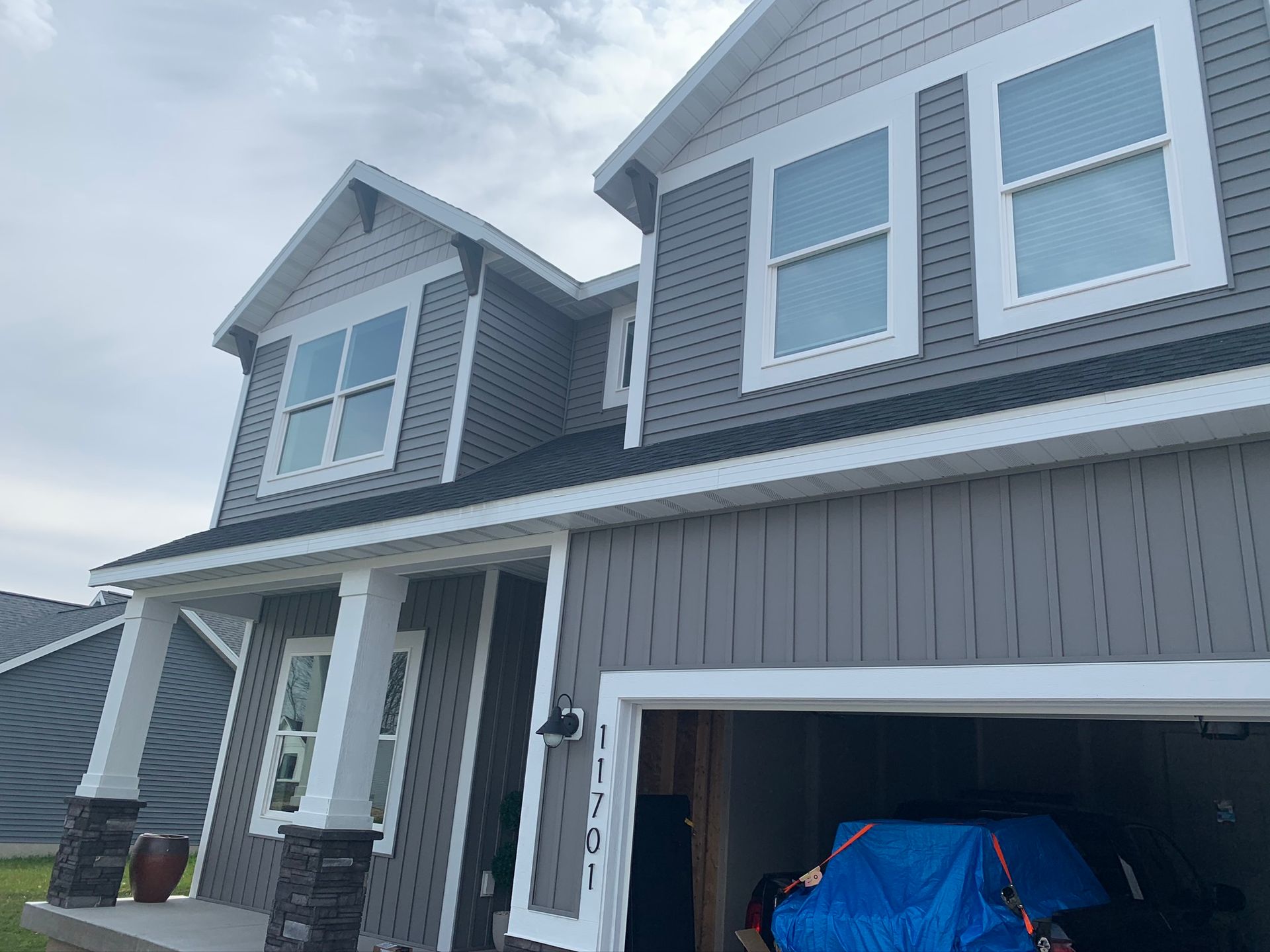 Gray two-story house with white trim, attached garage, and a blue car cover in the driveway.